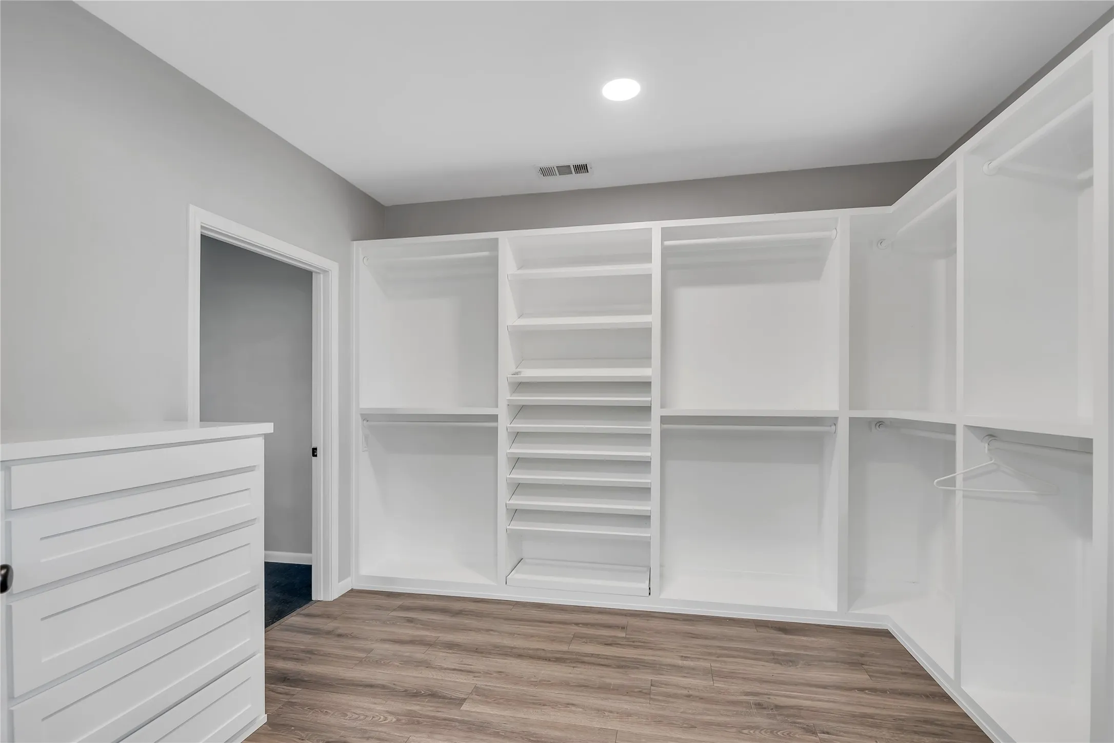 Built-in closet system featuring multiple hanging rods, adjustable shelving, and wood-finish flooring