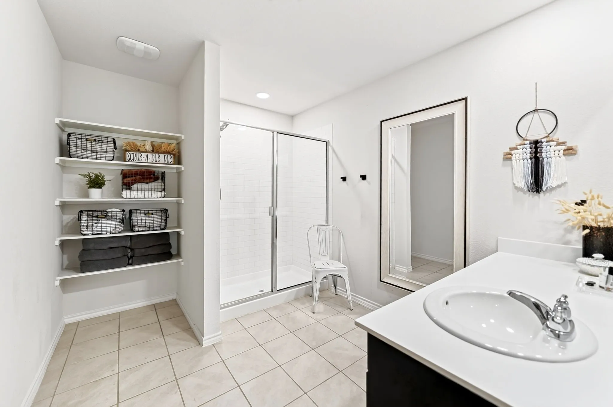 White tiled flooring, built-in shelving, glass-enclosed shower, single vanity with integrated sink, and wall-mounted mirror