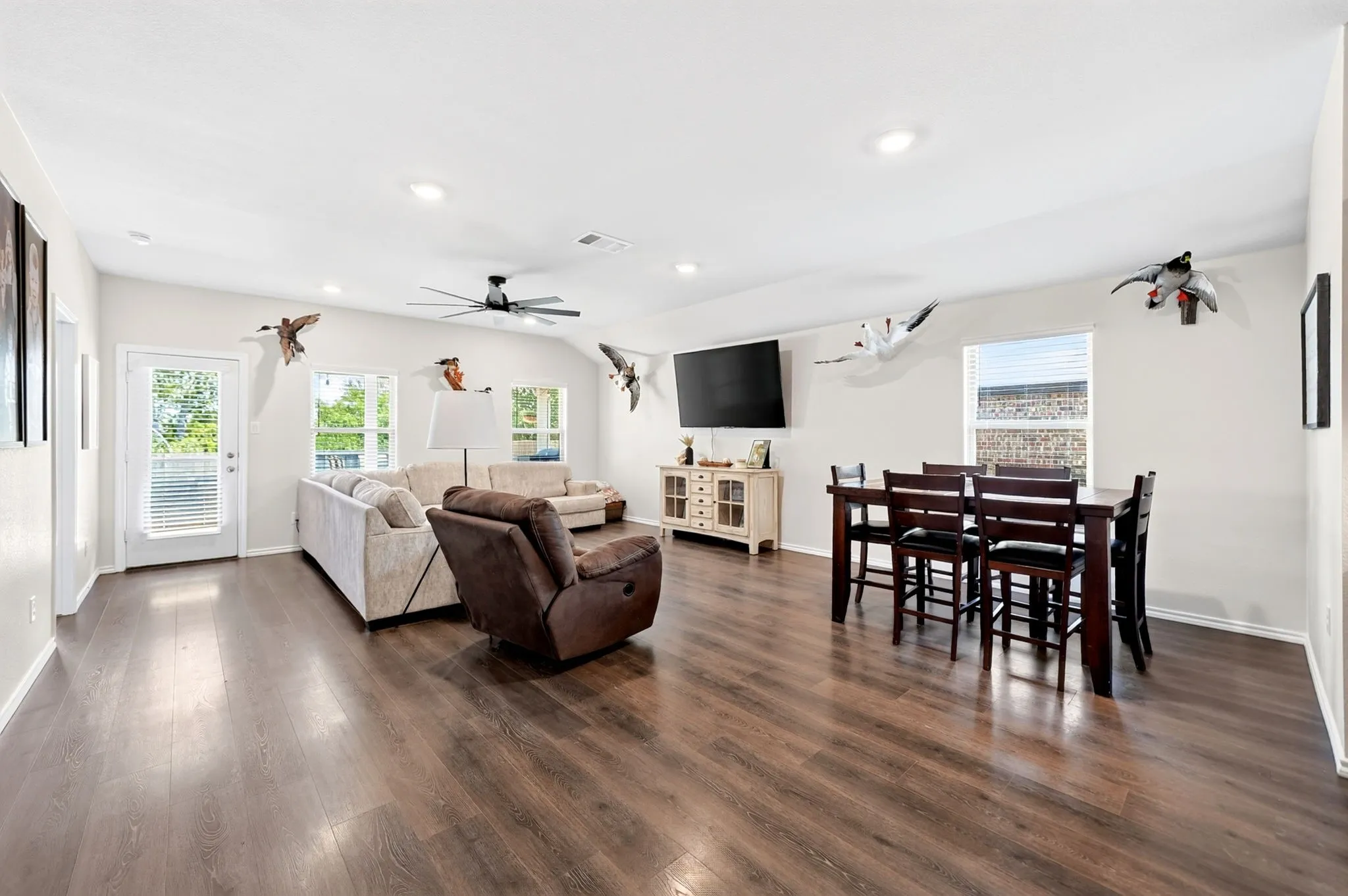 Vaulted ceiling with a ceiling fan, recessed lighting, wood-finish flooring, multiple windows with blinds, and a glass-paneled door
