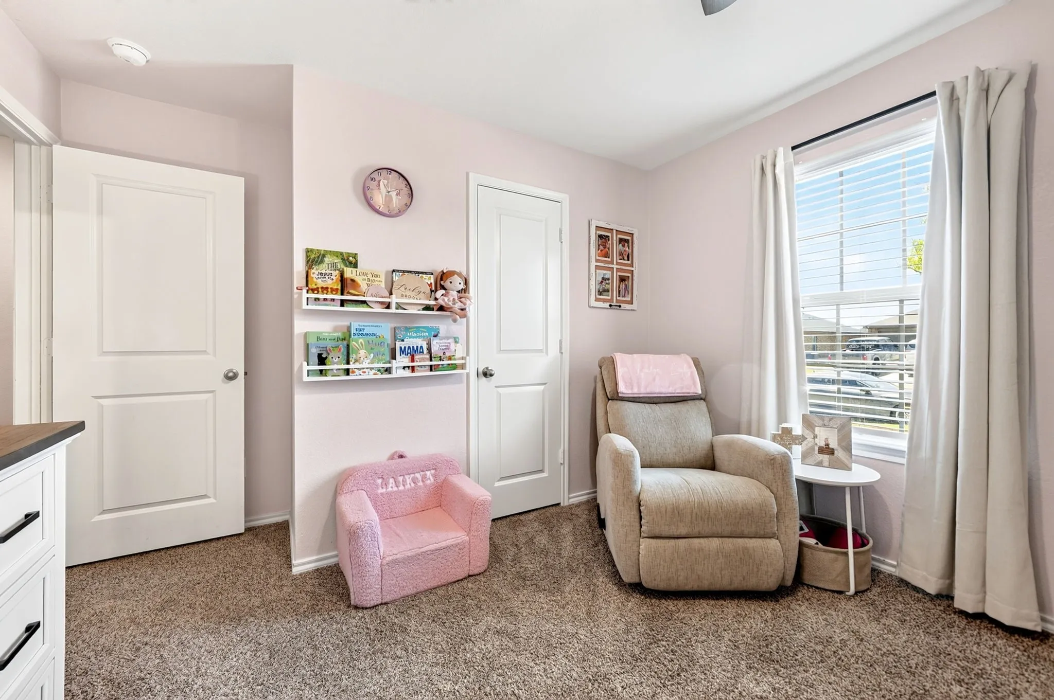 Plush carpeting, window with horizontal blinds, wall-mounted book shelving, and a ceiling fan