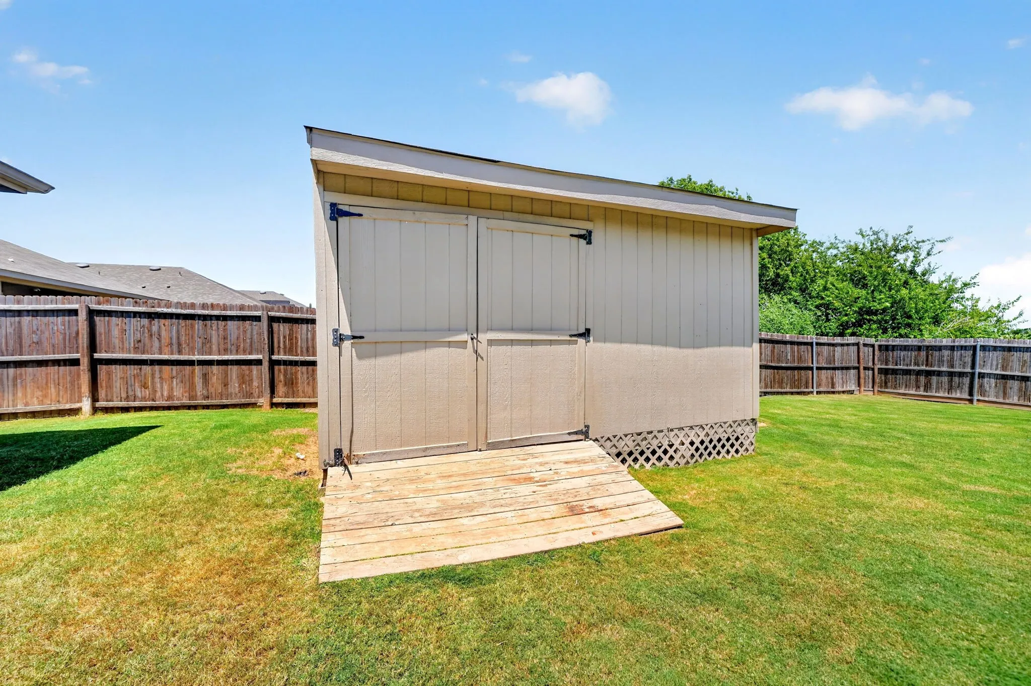 Backyard featuring a sloped shed with double doors, wood ramp, lattice skirting, and a wood privacy fence