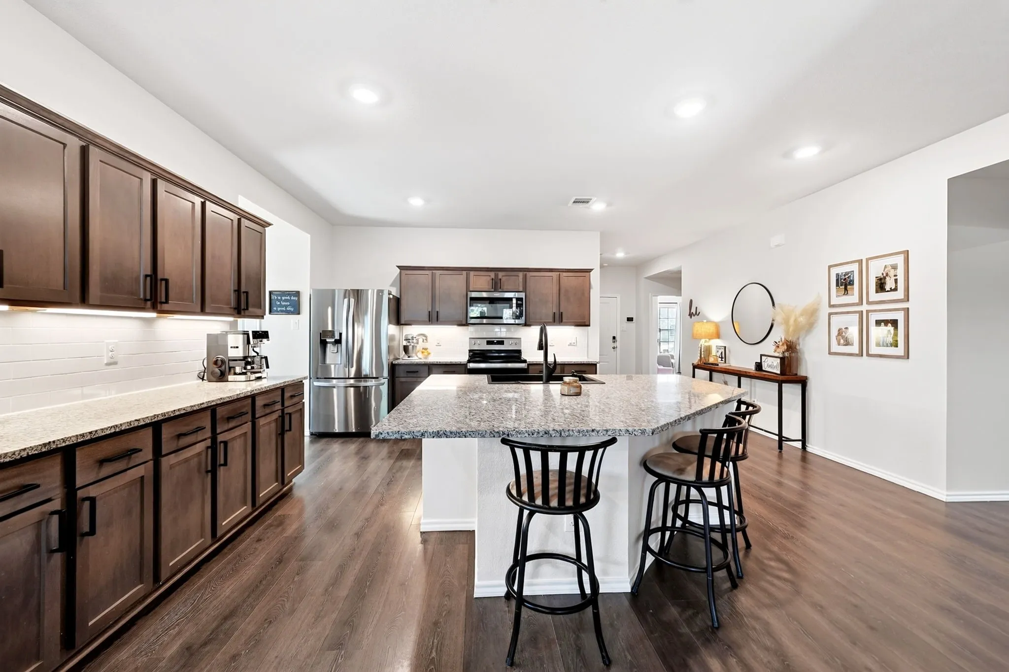 Spacious kitchen featuring an expansive central island with stone-finish countertop, dark wood-finish cabinetry, stainless steel appliances, and wood-finish flooring throughout