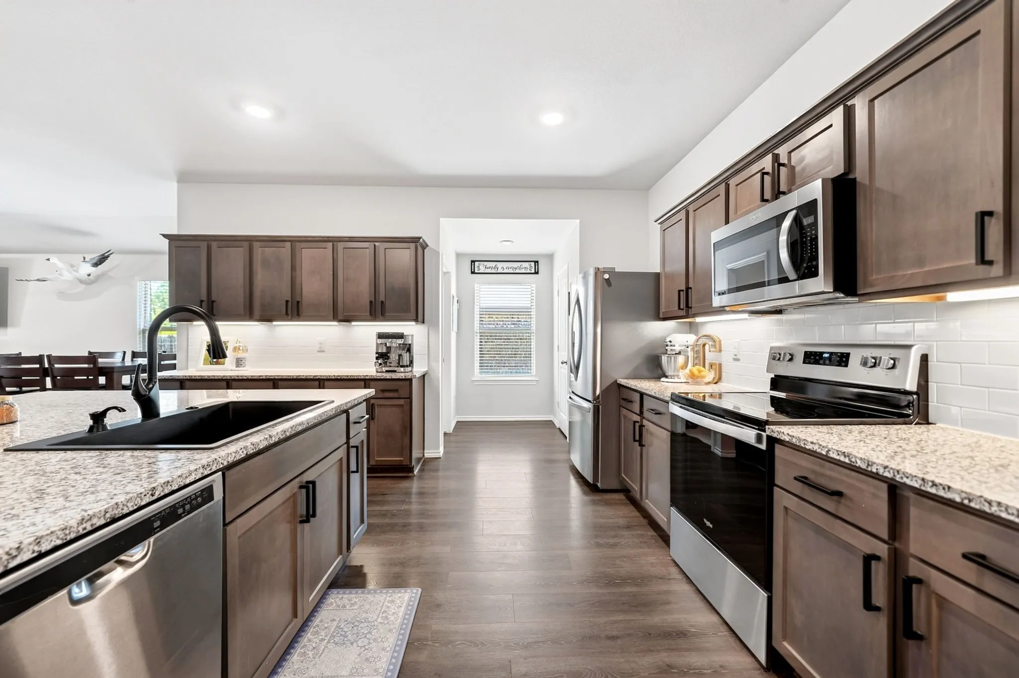 Spacious kitchen featuring wood-finish cabinetry, stainless steel appliances, speckled countertops, and a white subway tile backsplash