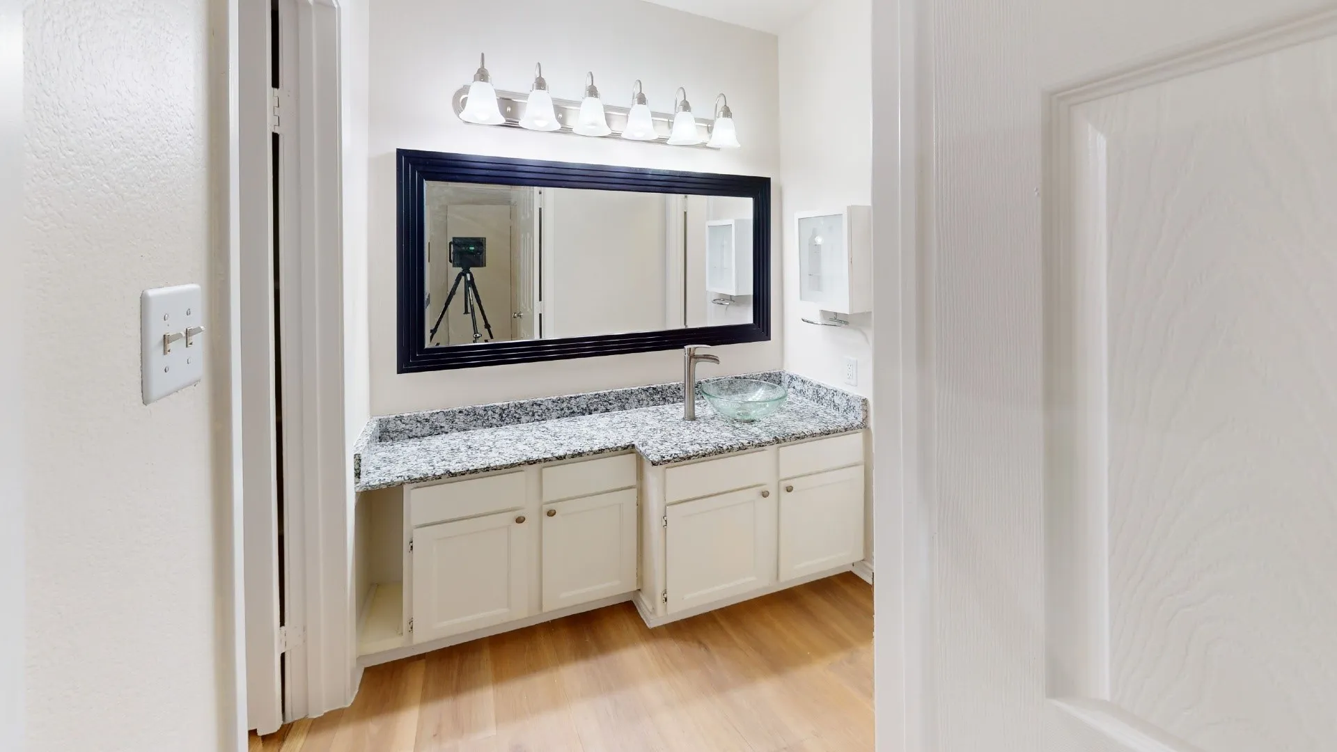Vanity with a framed mirror, granite-finish countertop, under-sink cabinetry, and wood-finish flooring