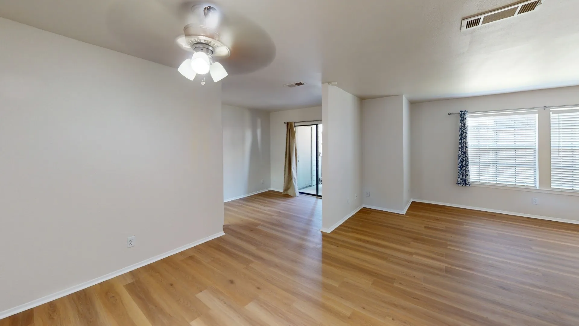 Spacious interior with wood-finish flooring, ceiling fan, and multiple windows with blinds
