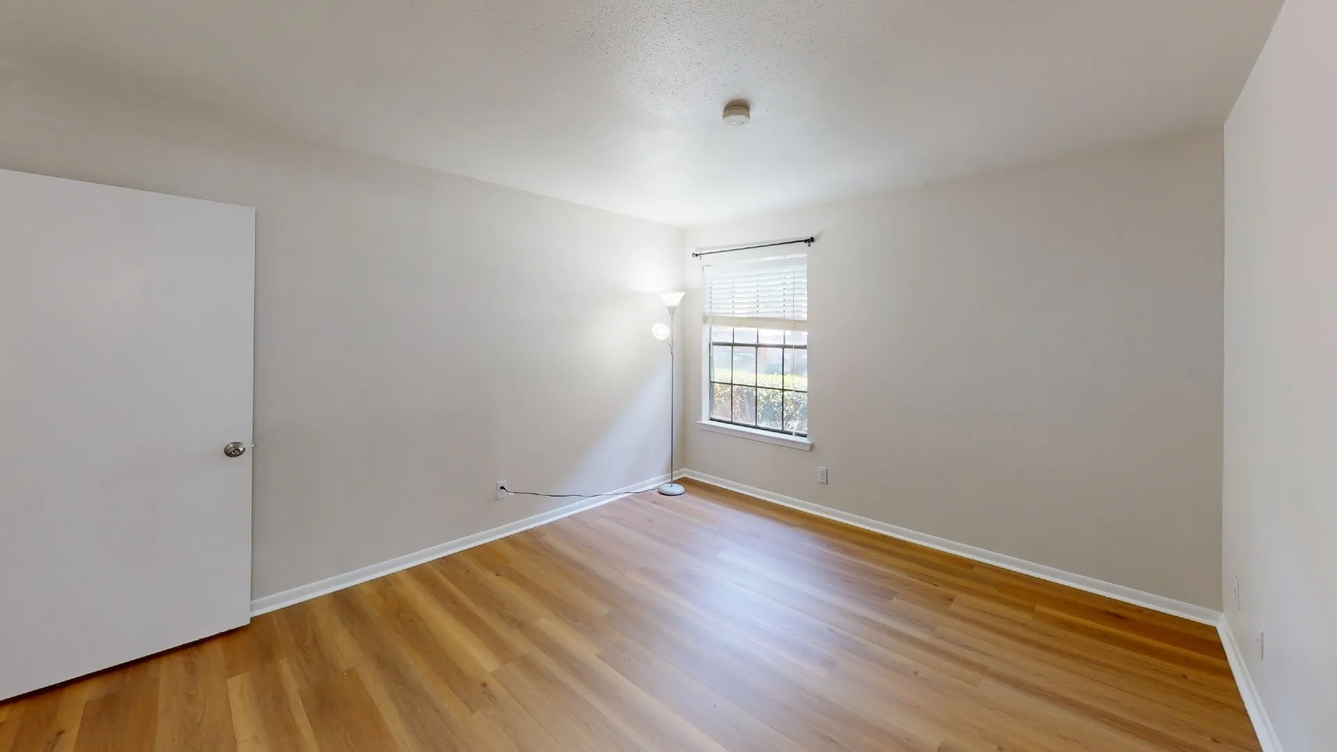 Wood-finish flooring with white baseboards, a window with horizontal blinds, and a white interior door