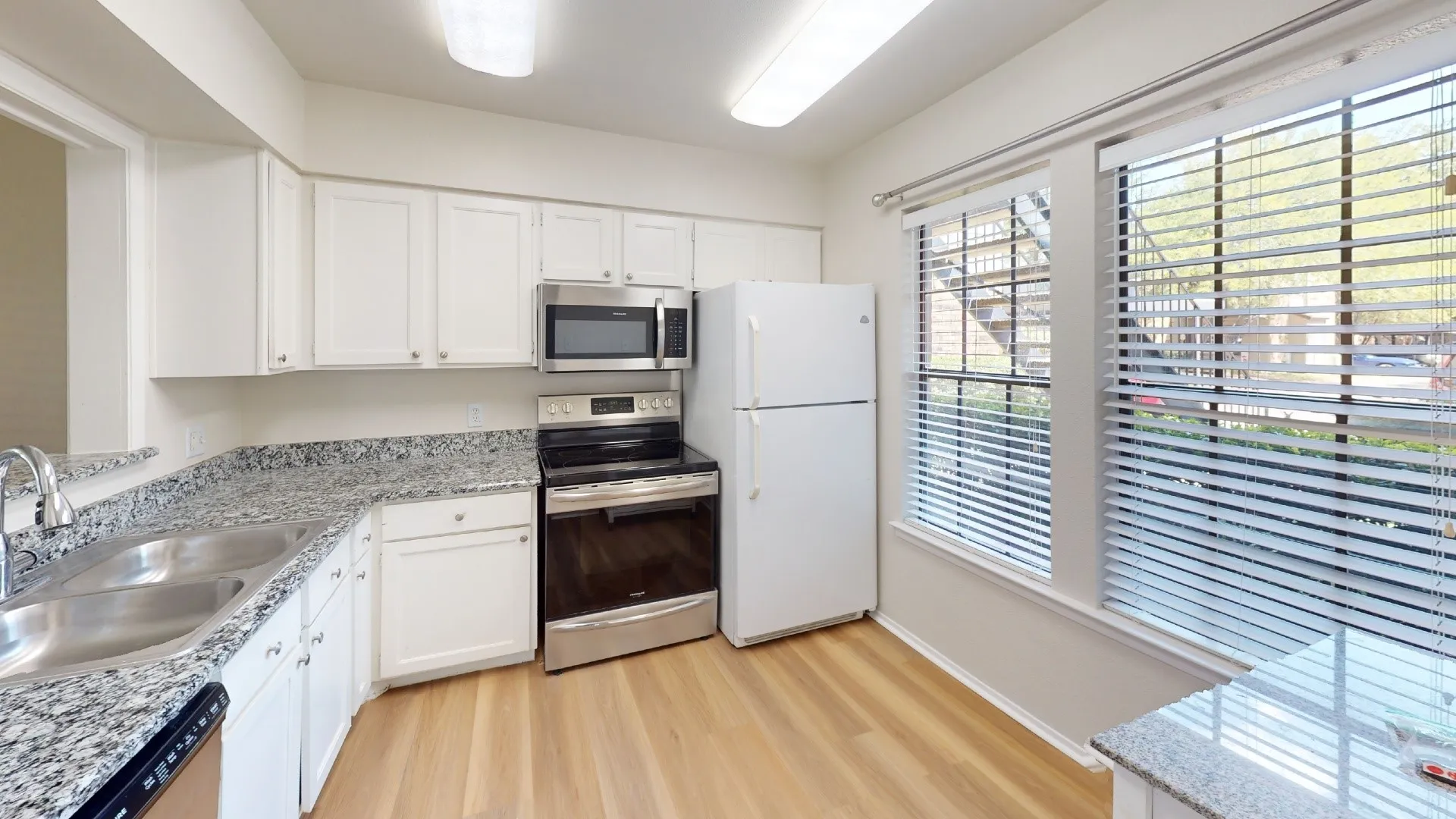 Kitchen featuring white cabinetry, wood-finish flooring, stainless steel appliances, and dual windows