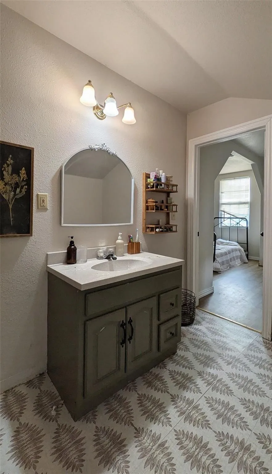 Vanity with integrated sink, arched mirror, three-light fixture, and patterned floor tiles