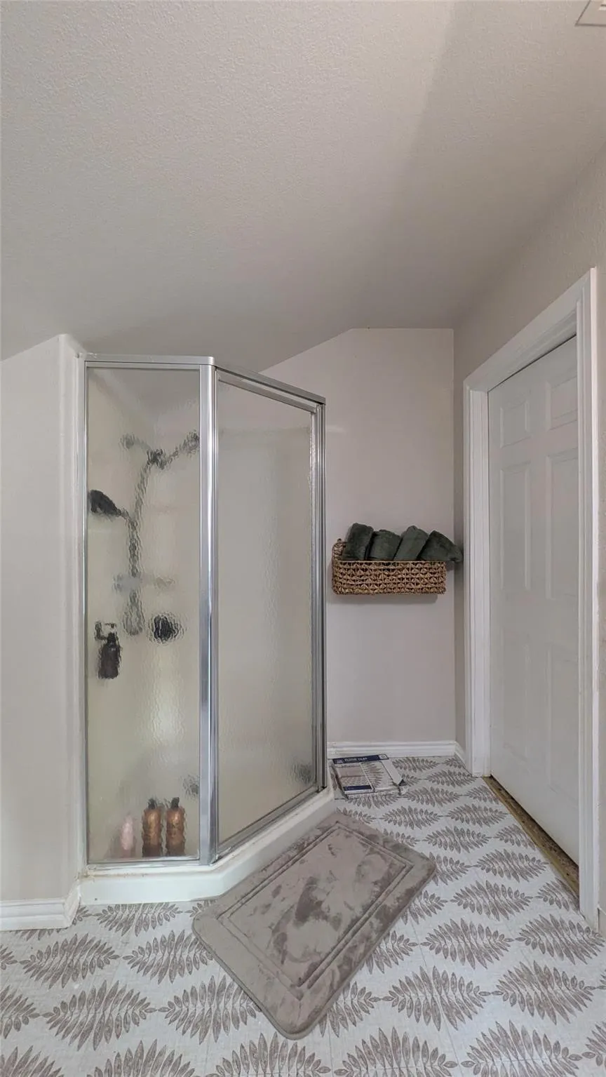Corner shower with a glass enclosure, white paneled door, and patterned floor