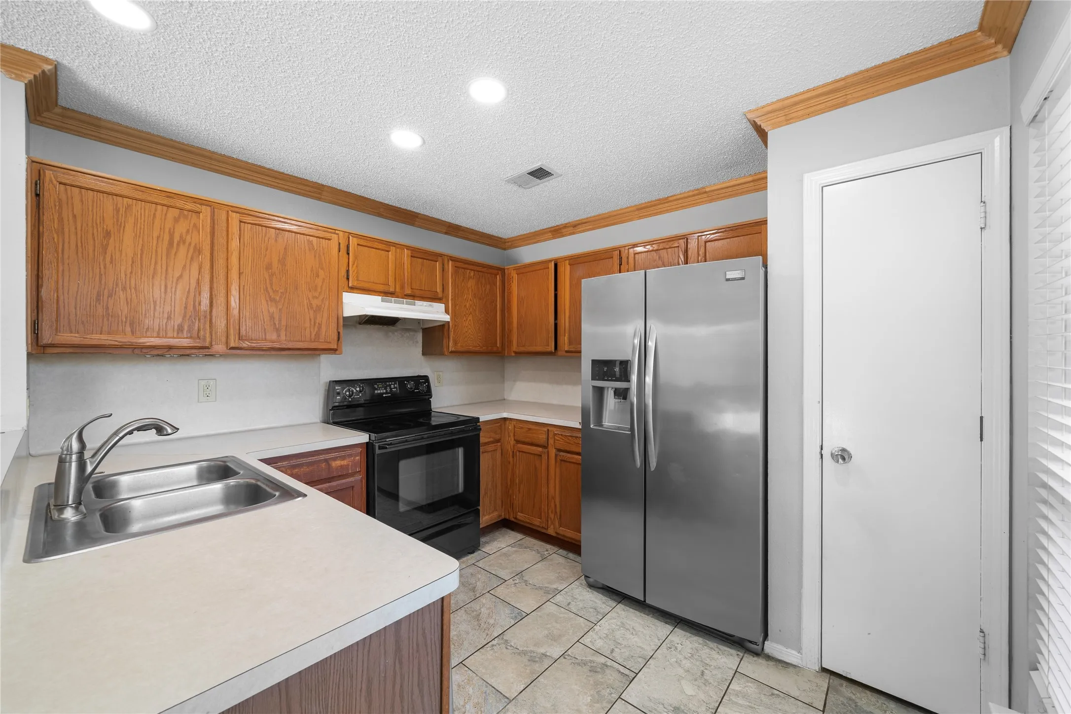 Kitchen featuring wood cabinetry, stainless steel refrigerator, black range, dual basin sink, and tile flooring