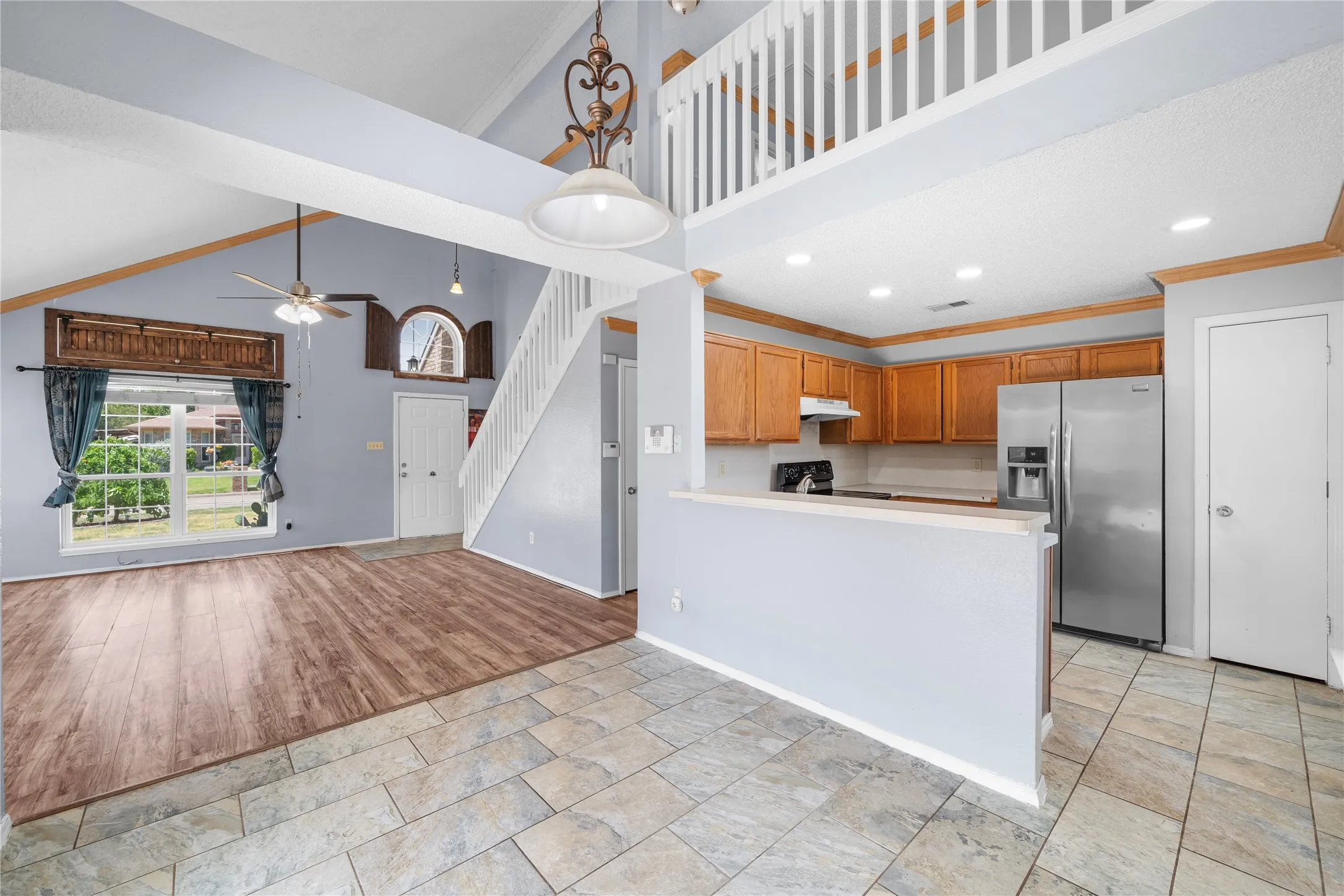 Vaulted ceiling with wood-finish beams, wood-finish flooring, kitchen with wood cabinetry, stainless steel refrigerator, and tiled flooring