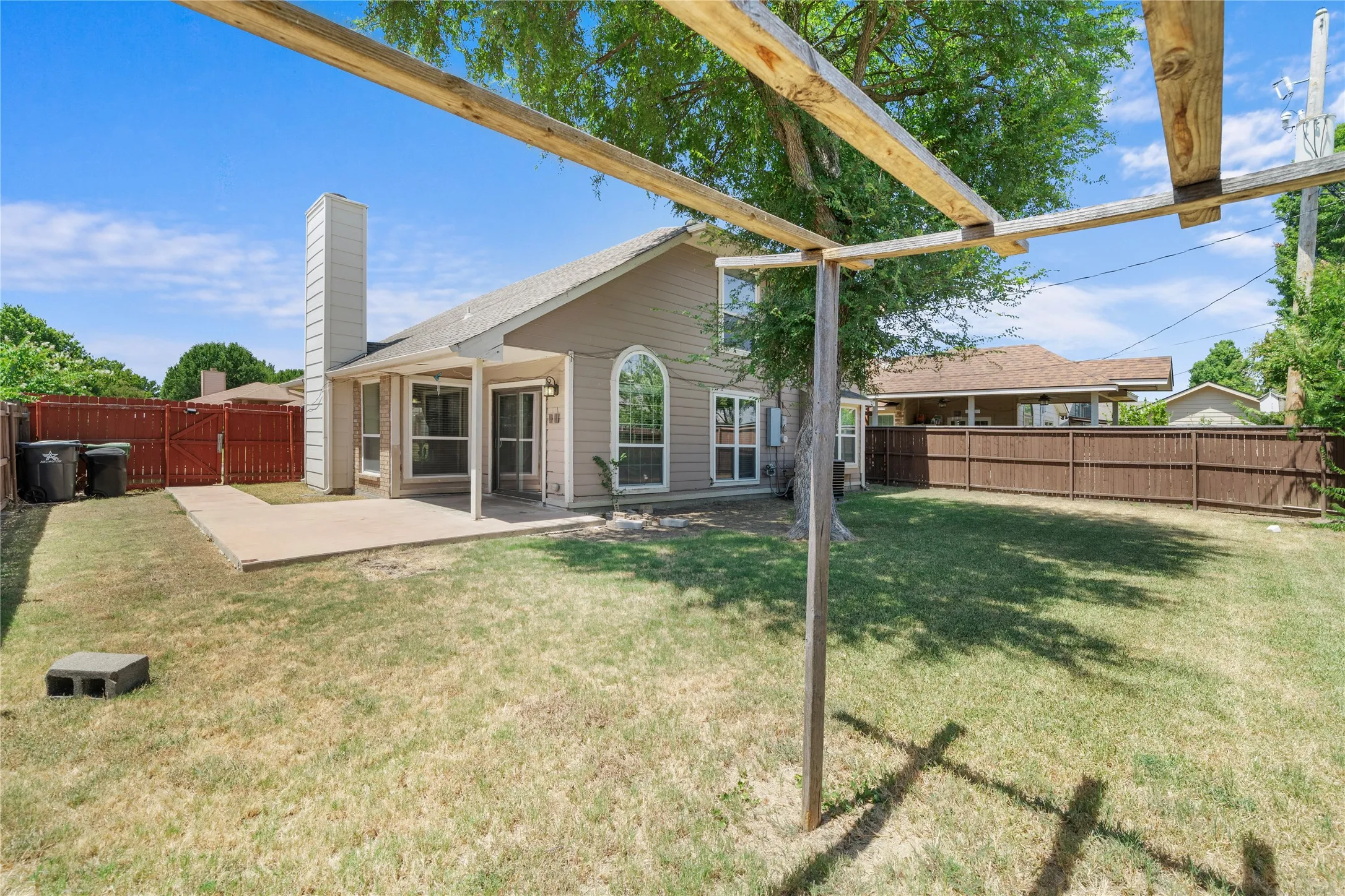 Expansive backyard featuring a concrete patio, wood fencing, mature trees, and a pergola structure
