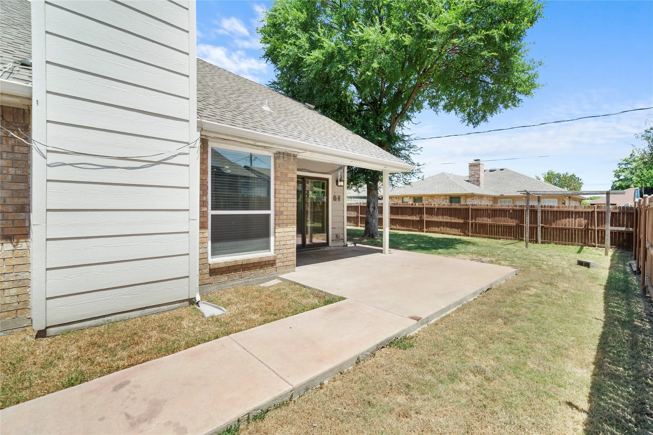 Covered concrete patio with access to the interior, complemented by a fenced perimeter and a grassy area