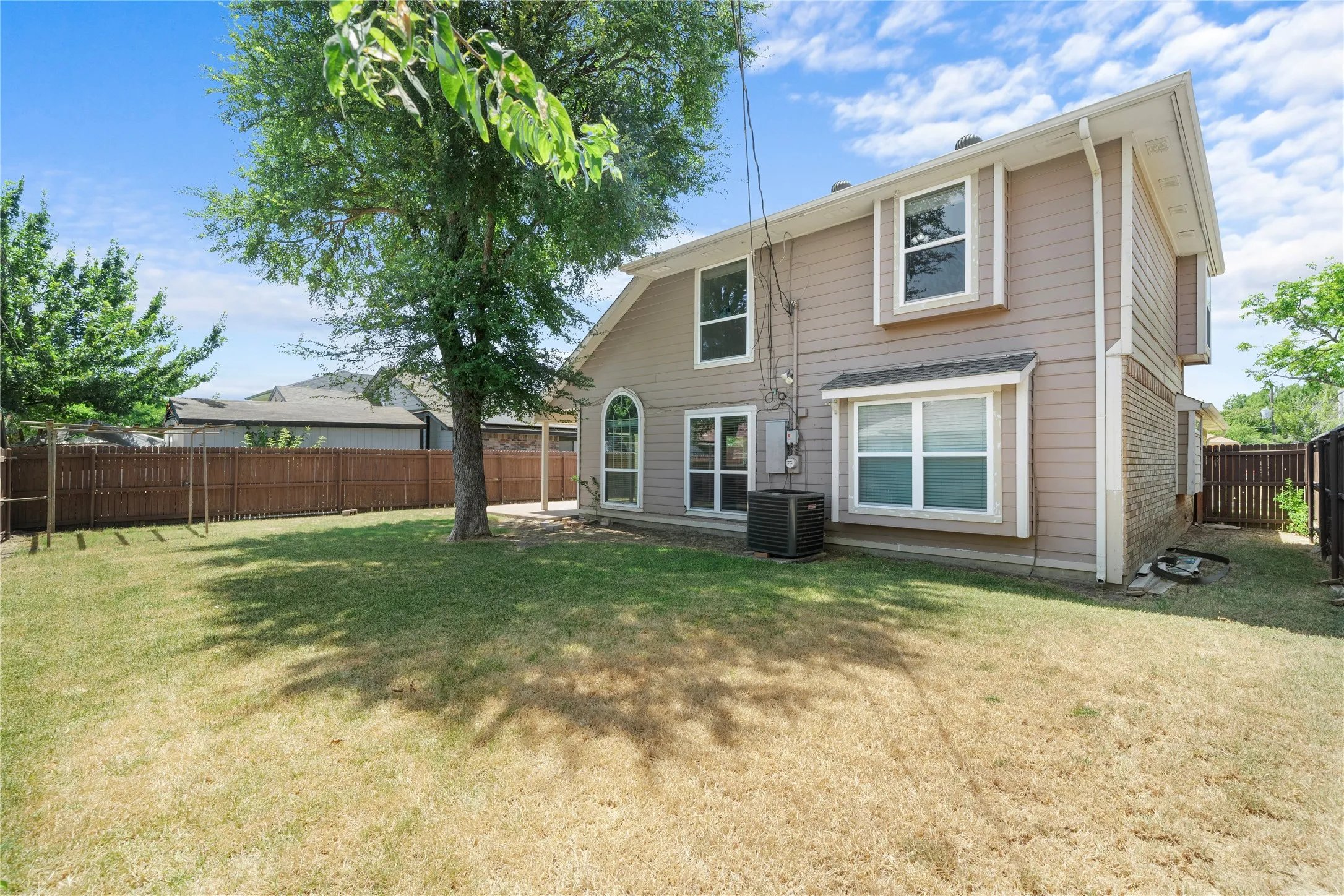 Fenced backyard with mature tree, side brick accent, and a ground-level patio