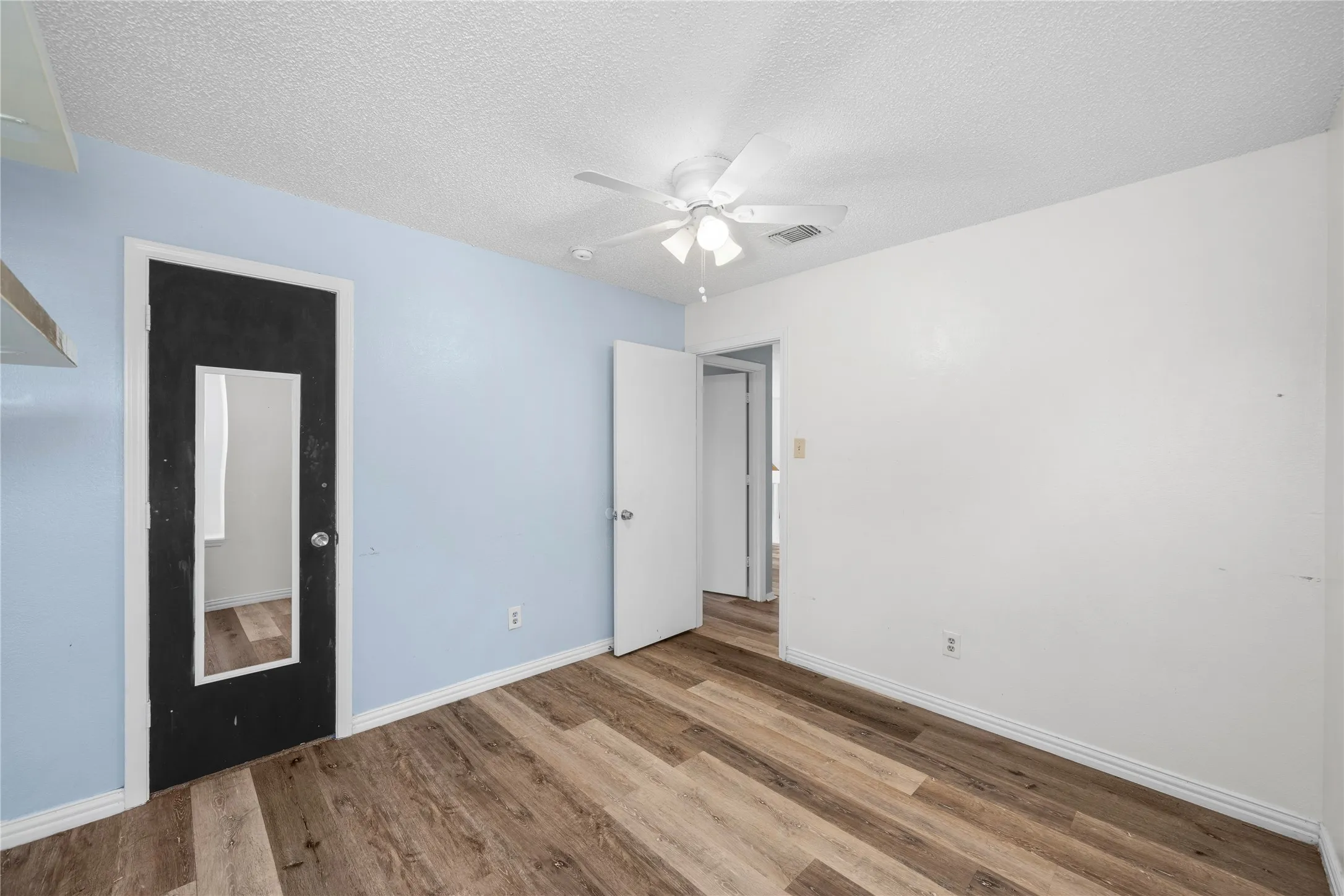 Wood-finish flooring, ceiling fan with light fixture, and black door with integrated mirror