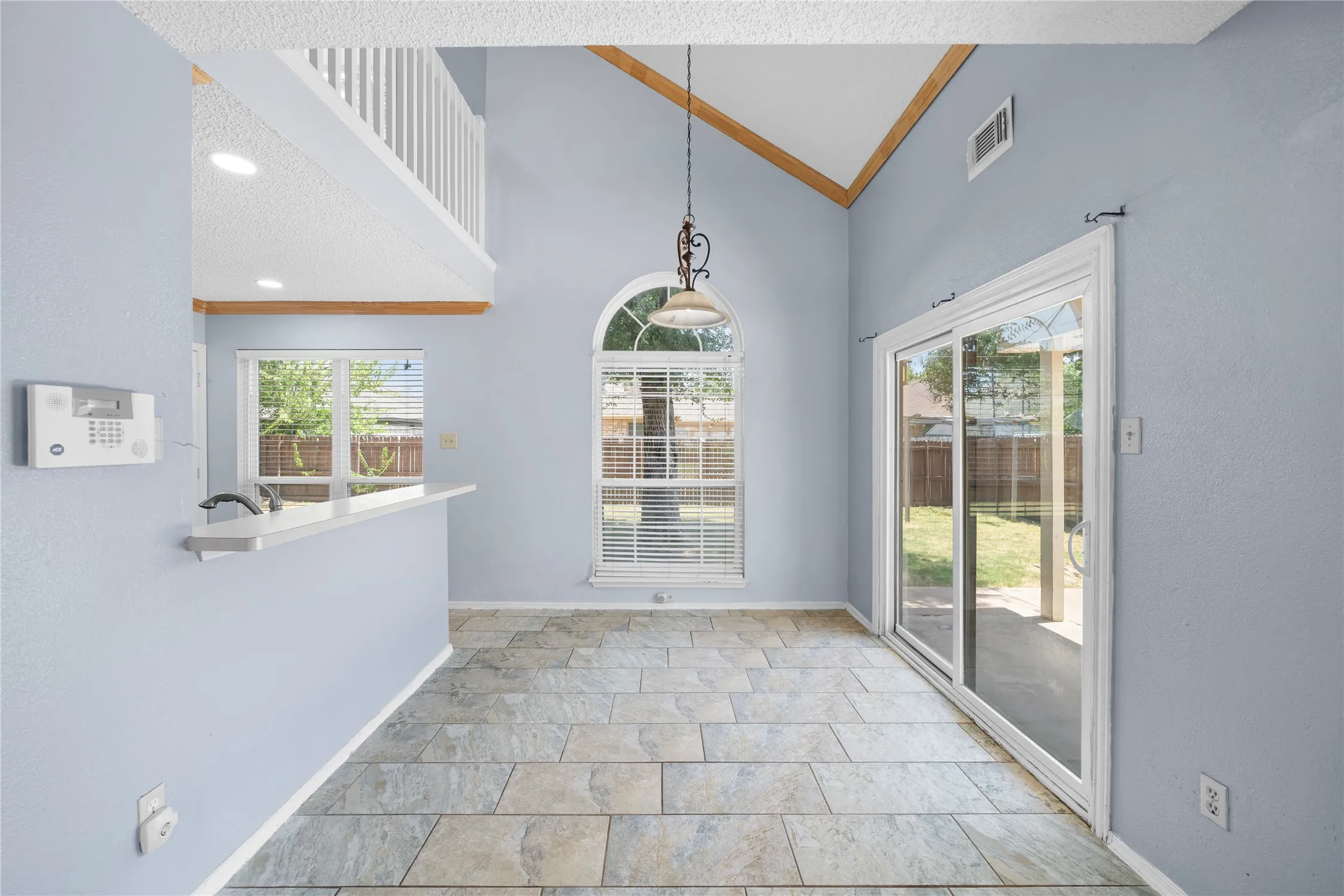 Vaulted ceiling with wood-finish trim, tile flooring, and a sliding glass door