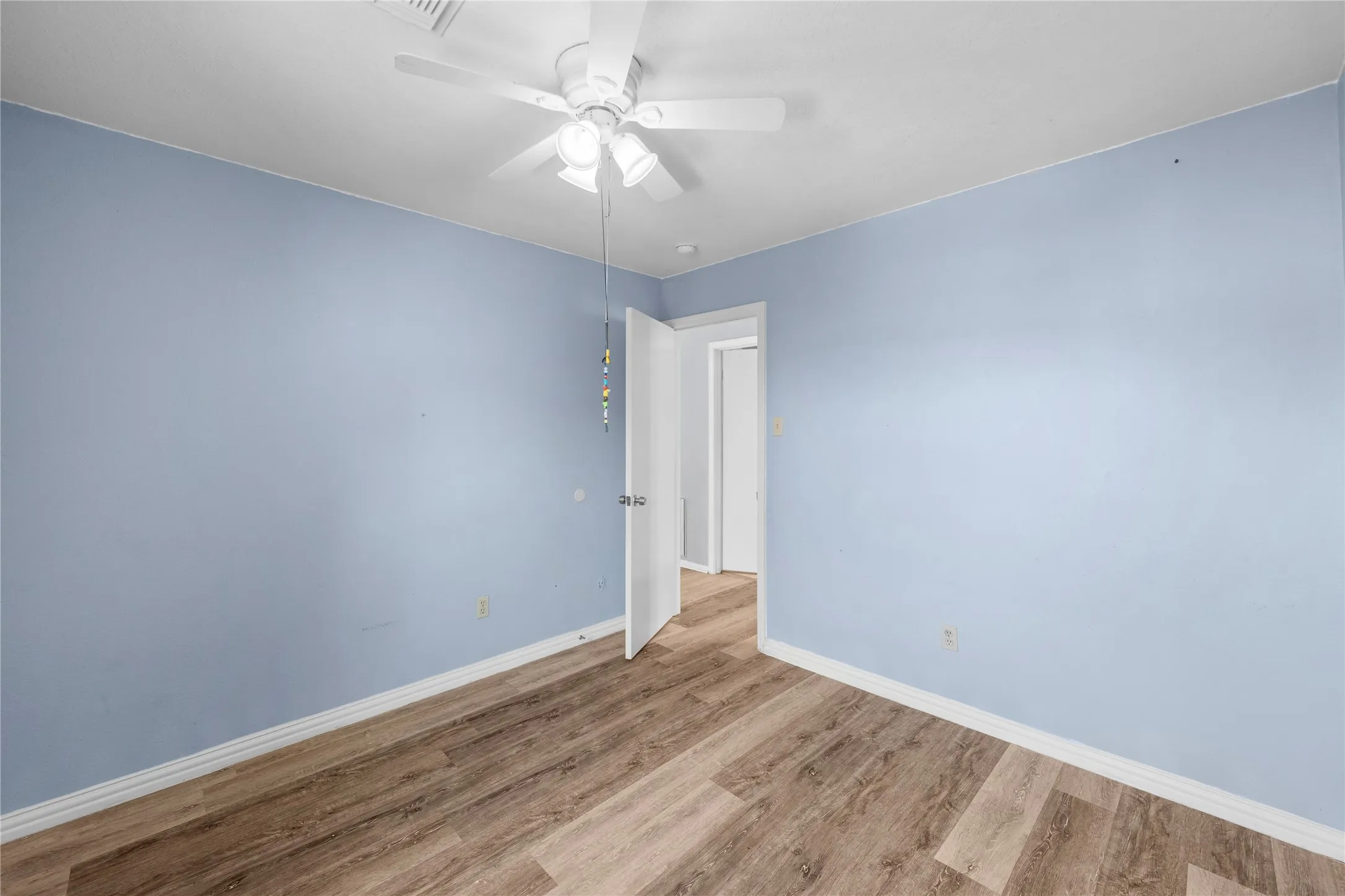 Wood-finish flooring with white trim and a ceiling fan with integrated lighting