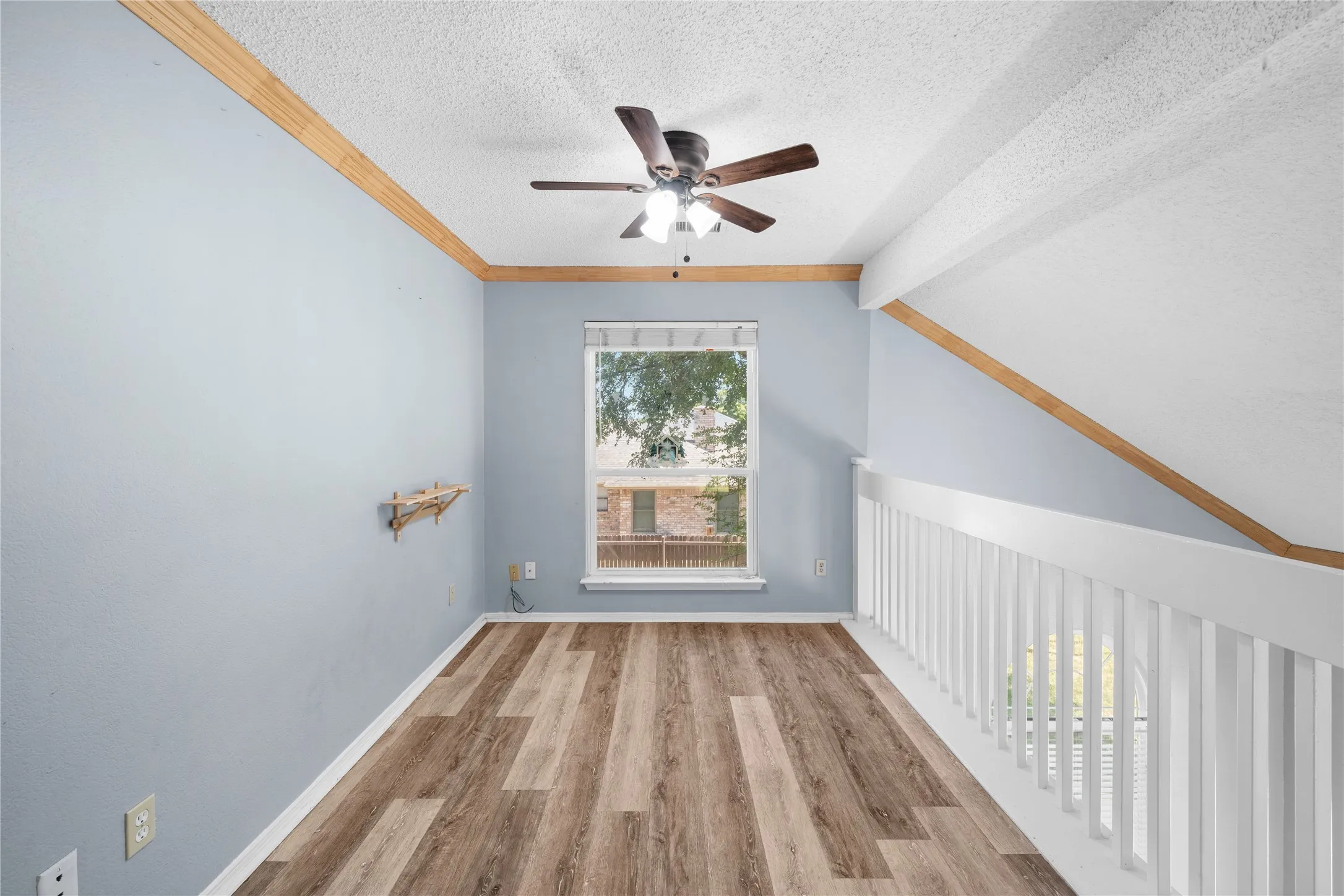 Wood-finish flooring, overhead ceiling fan, white window trim, and painted balusters