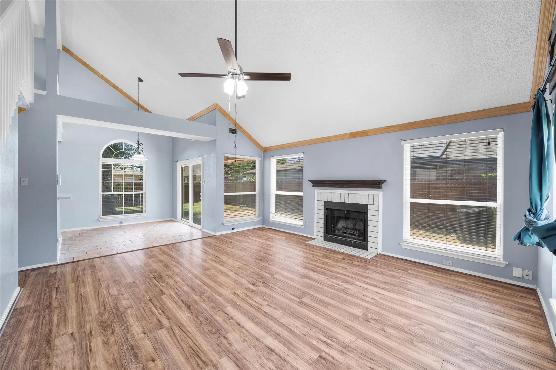 Vaulted ceiling with exposed wood beams, wood-finish flooring, brick fireplace with decorative mantel, multiple windows, and patio doors