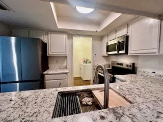 Kitchen with a raised ceiling, stainless steel appliances, white cabinets, and light stone countertops