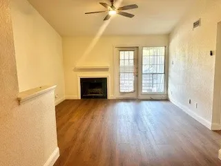 Unfurnished living room featuring a textured wall, wood finished floors, a fireplace, and a ceiling fan