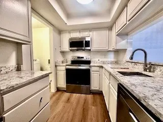 Kitchen featuring a tray ceiling, stainless steel appliances, wood finished floors, and white cabinetry