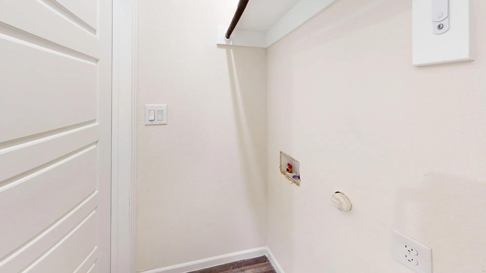 Dedicated utility space featuring a neutral color palette, wood-finish flooring, and a built-in hanging rod