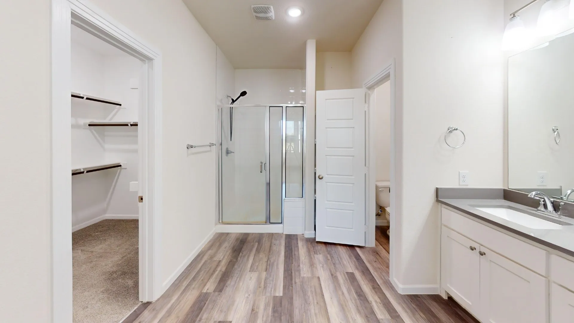 Wood-finish flooring, walk-in shower with glass enclosure, dual vanity with undermount sinks, and a dedicated water closet