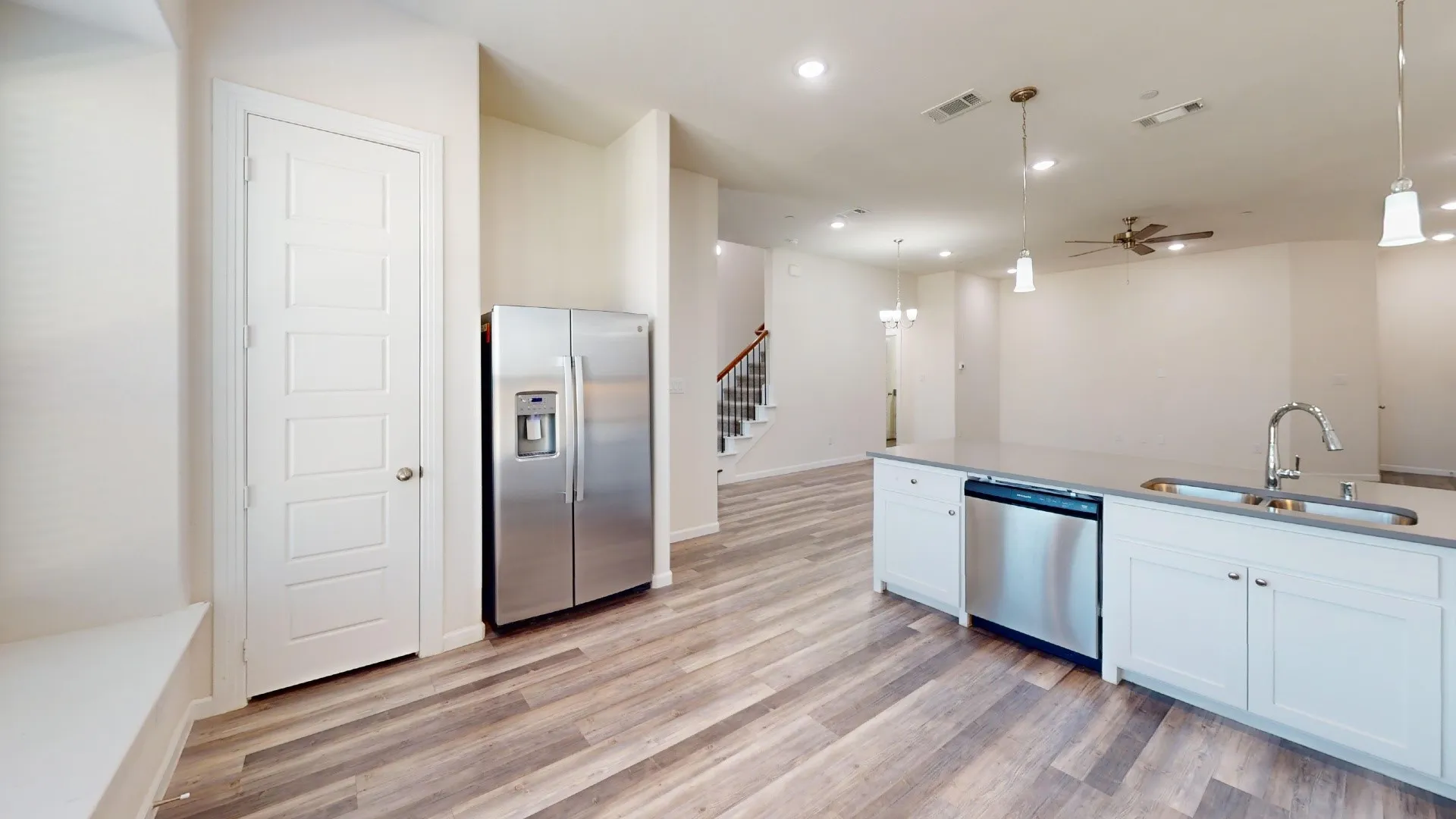 Open-concept living area with wood-finish flooring, white cabinetry, stainless steel appliances, and recessed lighting
