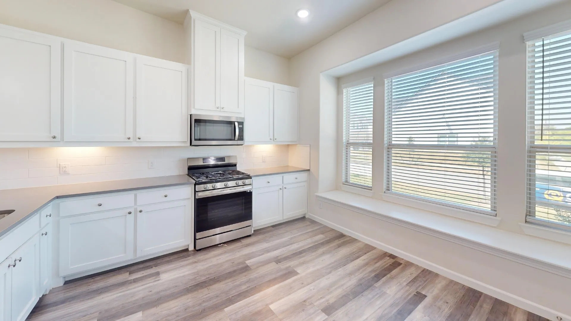 Wood-finish flooring, white cabinetry, stainless steel appliances, grey countertops, and a built-in window bench