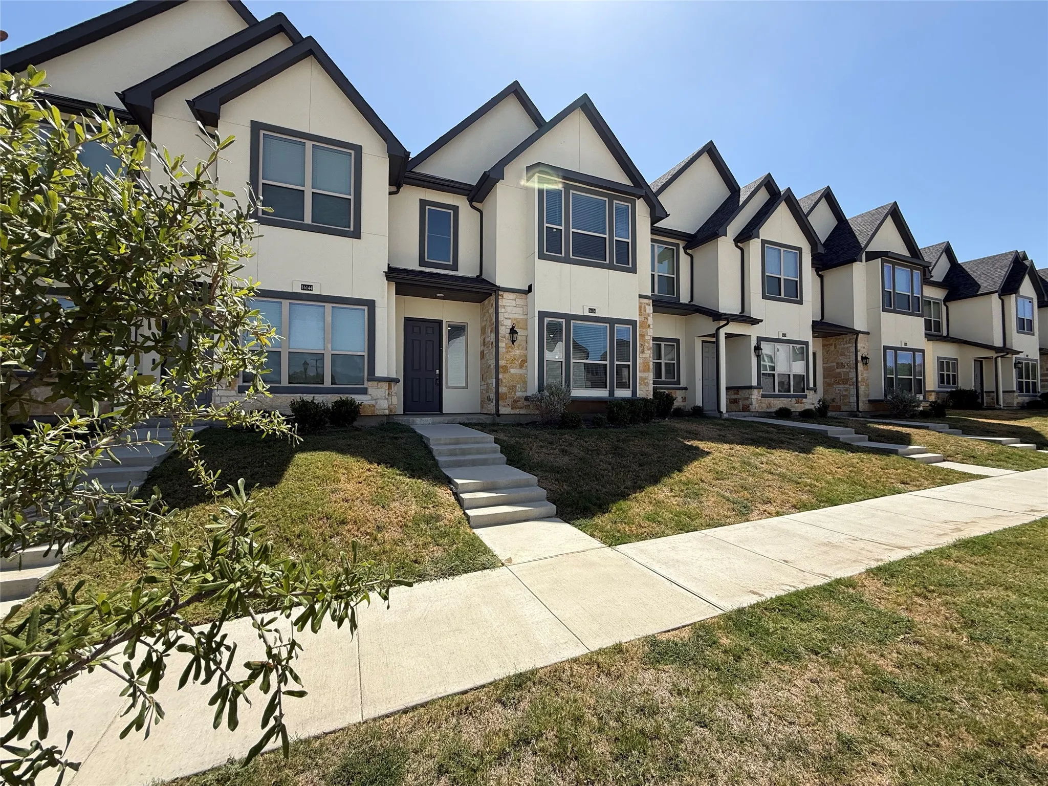 Modern townhome with gabled roofline, light-colored siding, stone accents, dark trim, and a concrete walkway