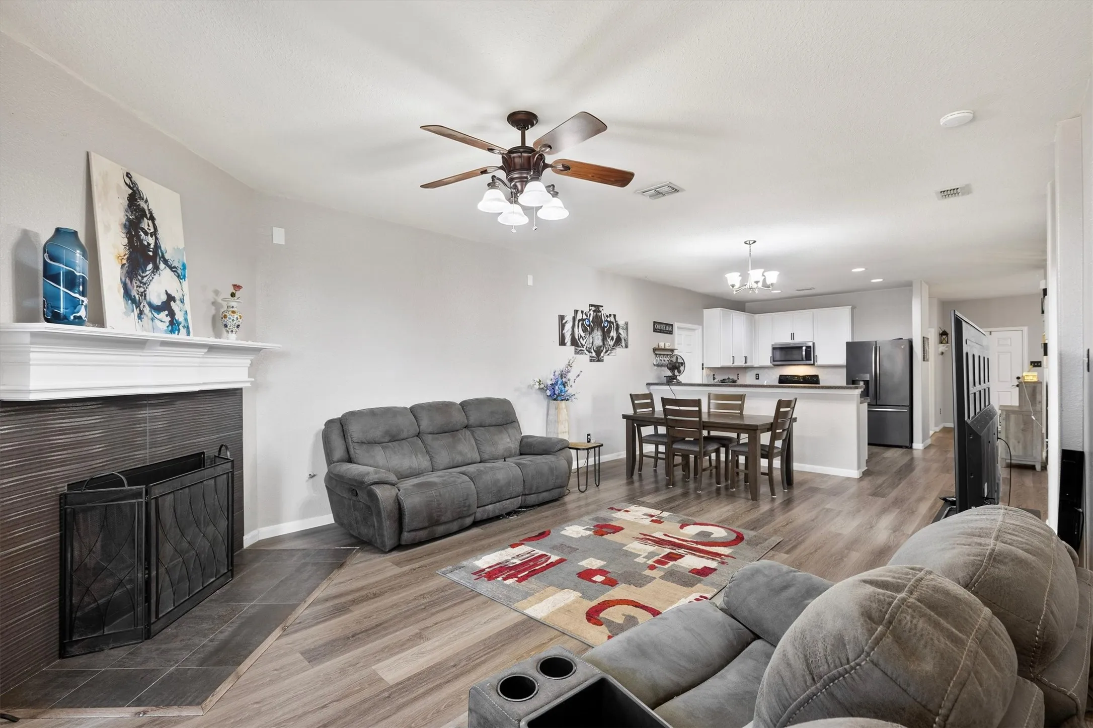 Living area featuring wood-finish flooring, a ceiling fan with integrated lighting, and a fireplace with a white mantel and tile surround