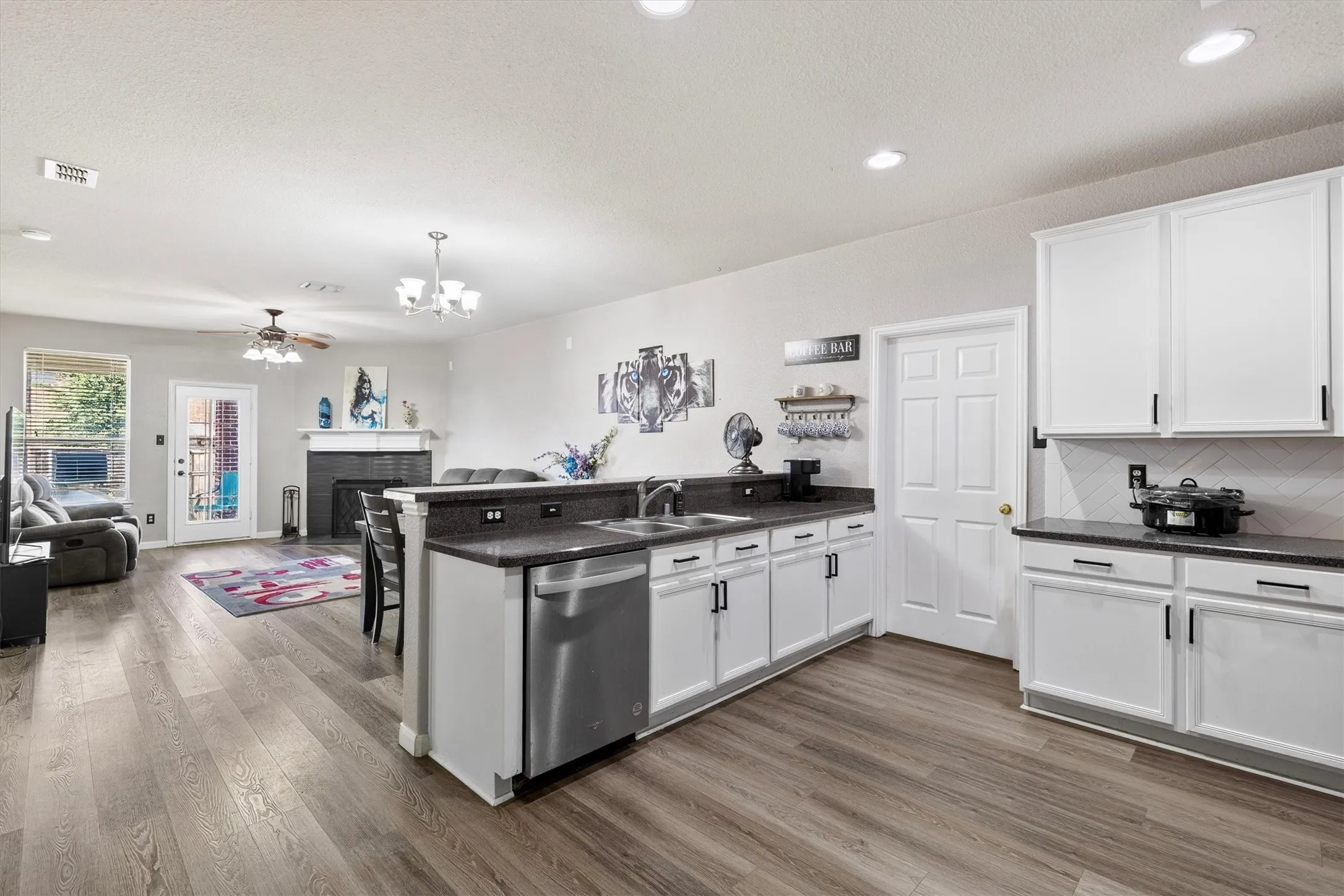 Open-concept living space with wood-finish flooring, recessed lighting, and a white kitchen featuring dark countertops and stainless steel appliances