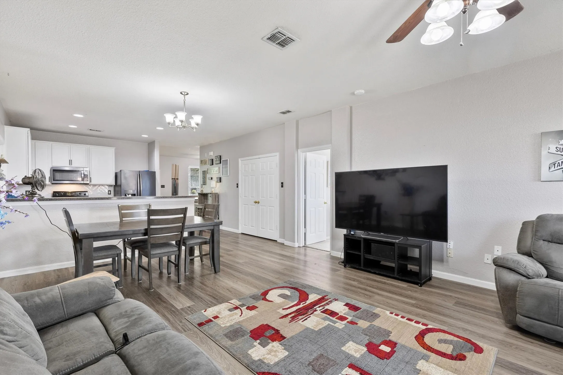 Wood-finish flooring throughout, ceiling fan with integrated lighting, recessed lighting, white cabinetry, and stainless steel appliances