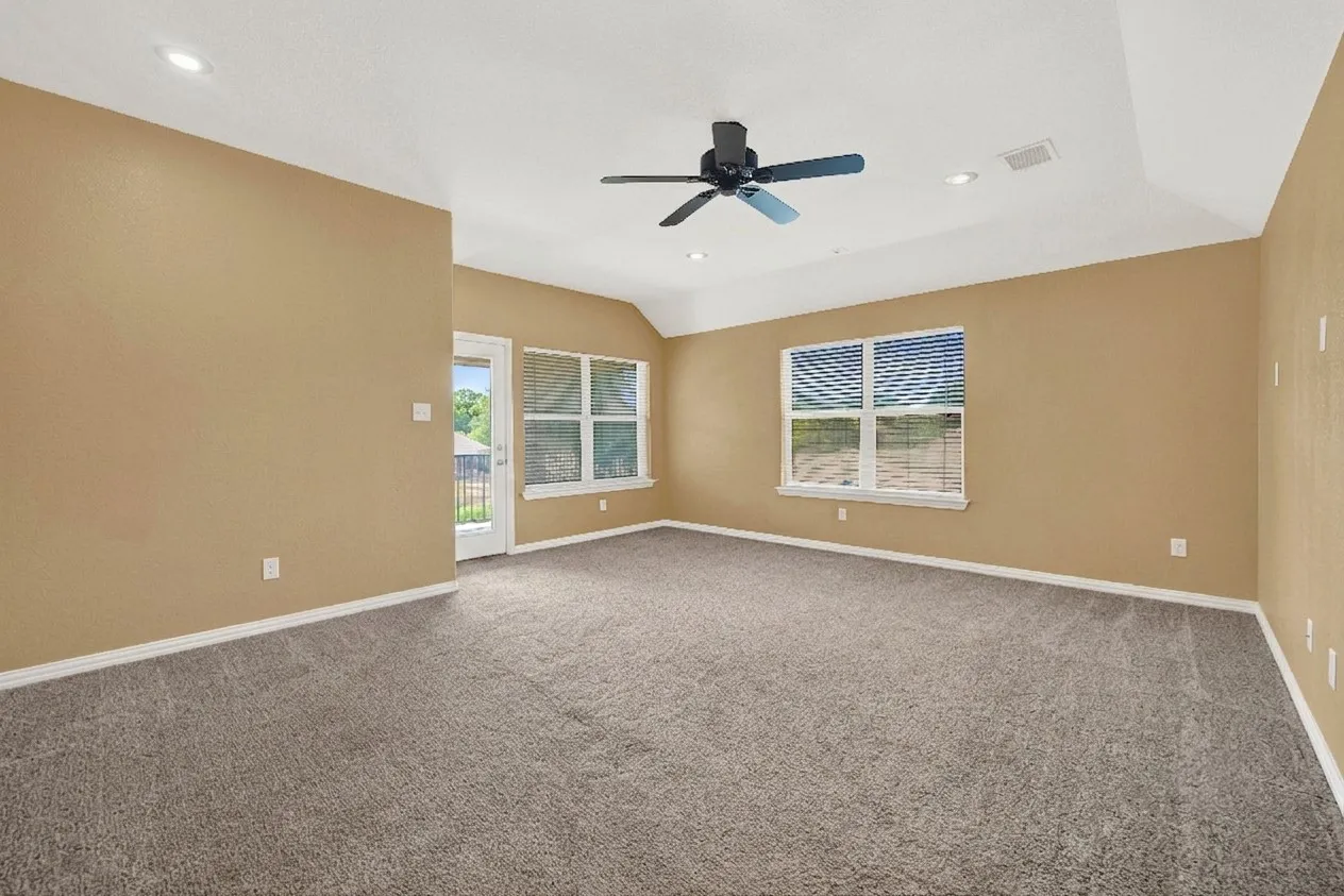 Spacious room featuring carpeting, tray ceiling, recessed lighting, ceiling fan, and large windows with blinds