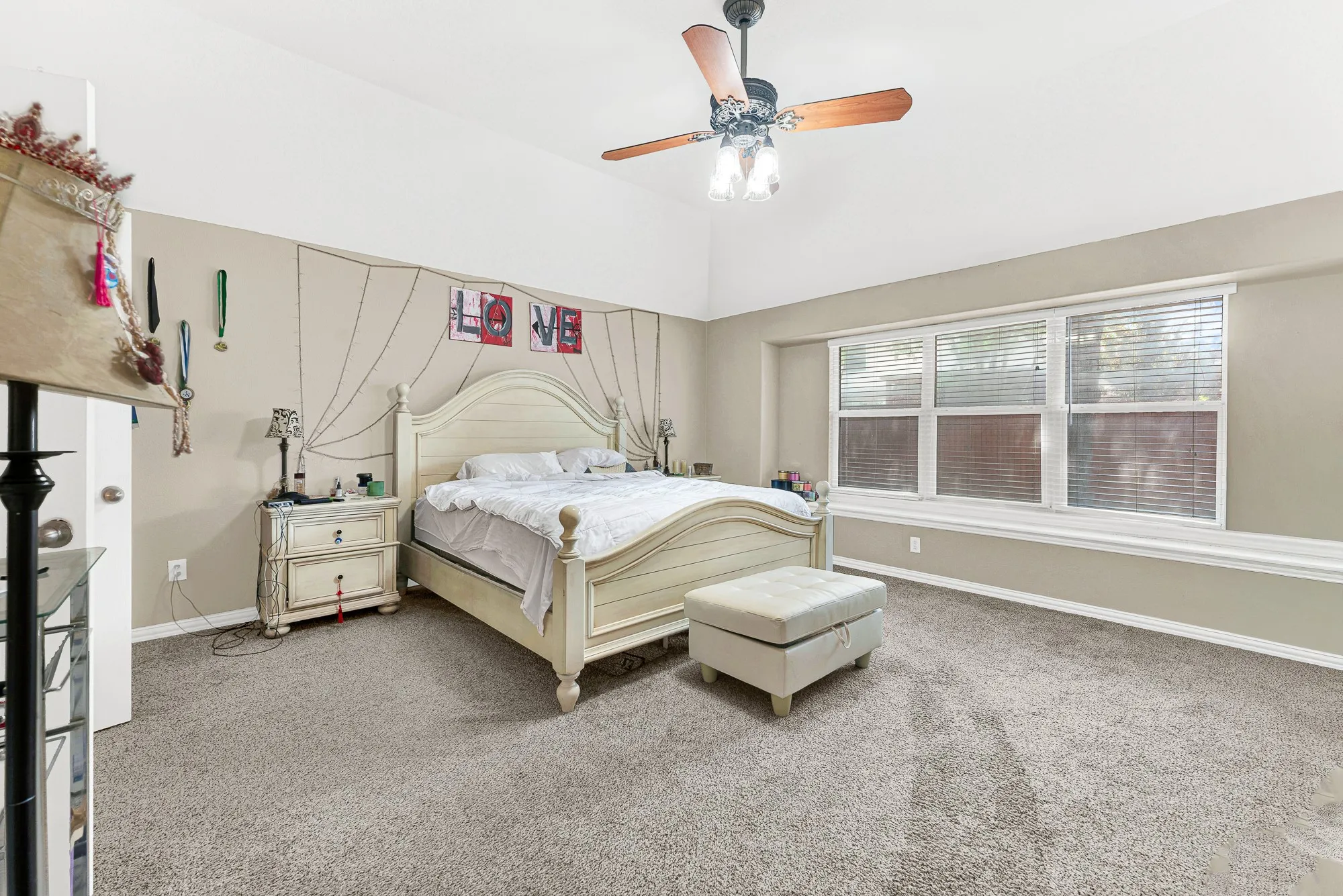Vaulted ceiling with a ceiling fan, broad window with white trim, and light-colored carpeting