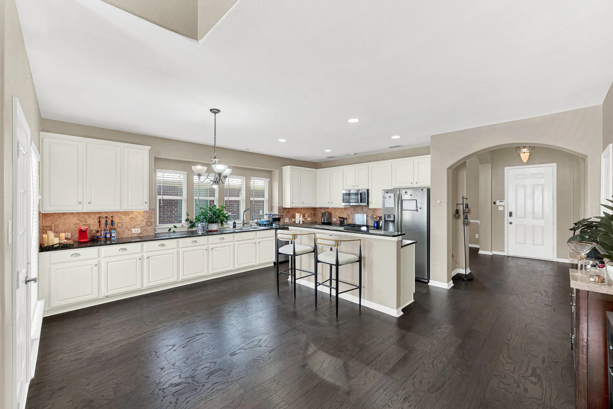 Open-concept kitchen featuring dark wood-finish flooring, white cabinetry, dark countertops, and stainless steel appliances