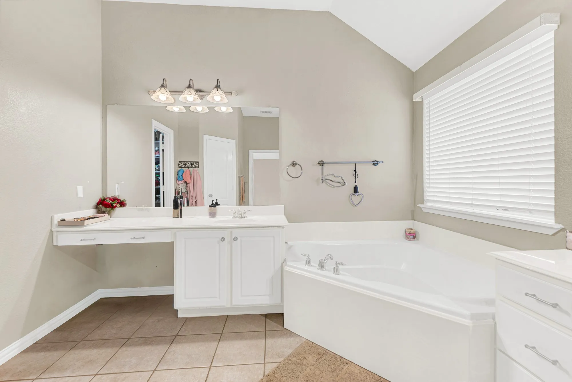 Corner soaking tub, dual-sink vanity with white cabinetry, tile flooring, and vaulted ceiling