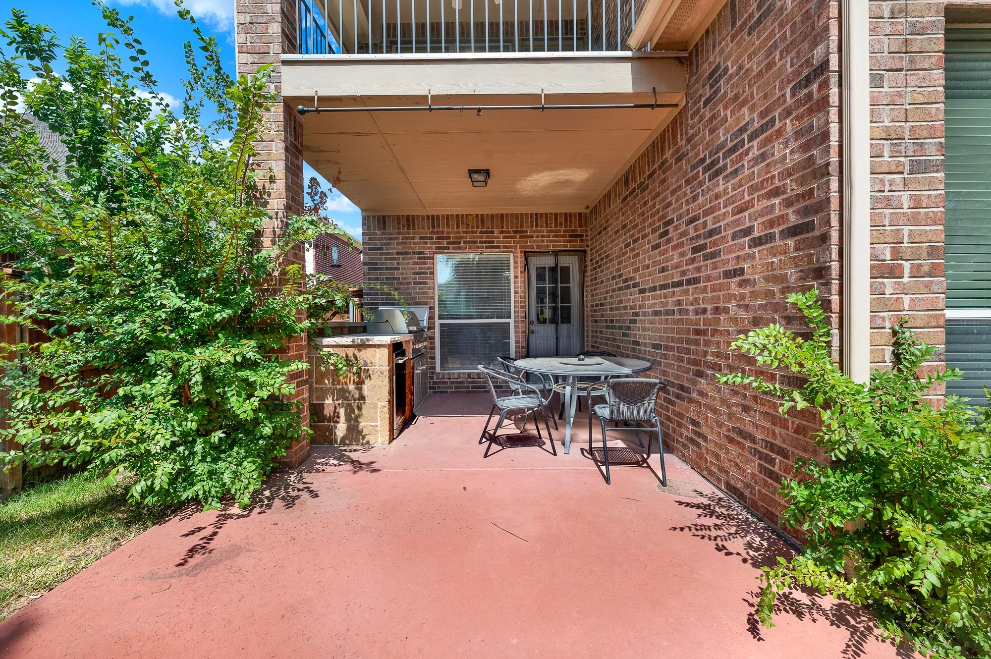 Covered patio featuring a built-in outdoor kitchen, brick-finish exterior, and mature landscaping