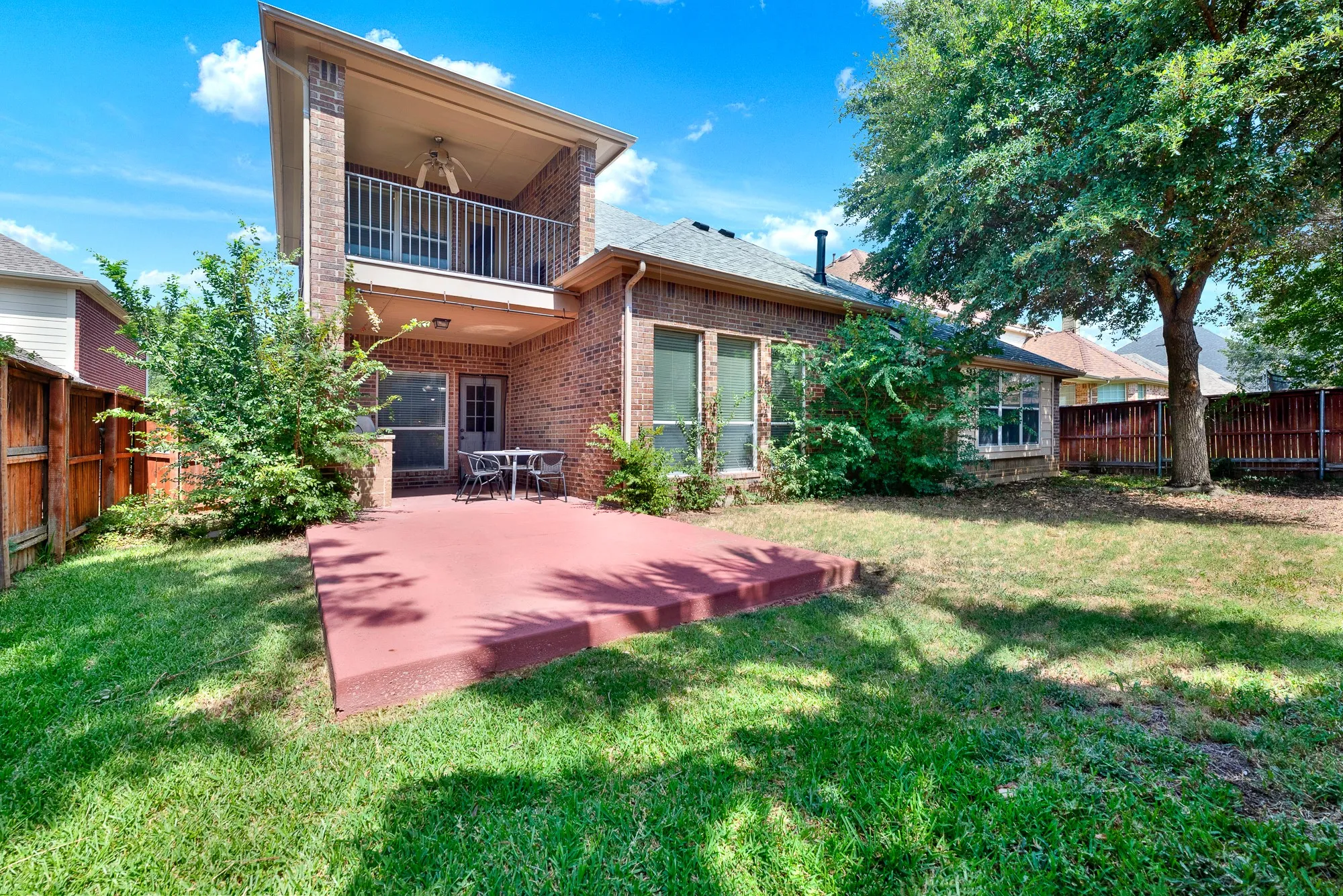 Expansive backyard featuring a manicured lawn, a large mature tree, and a red-toned concrete patio
