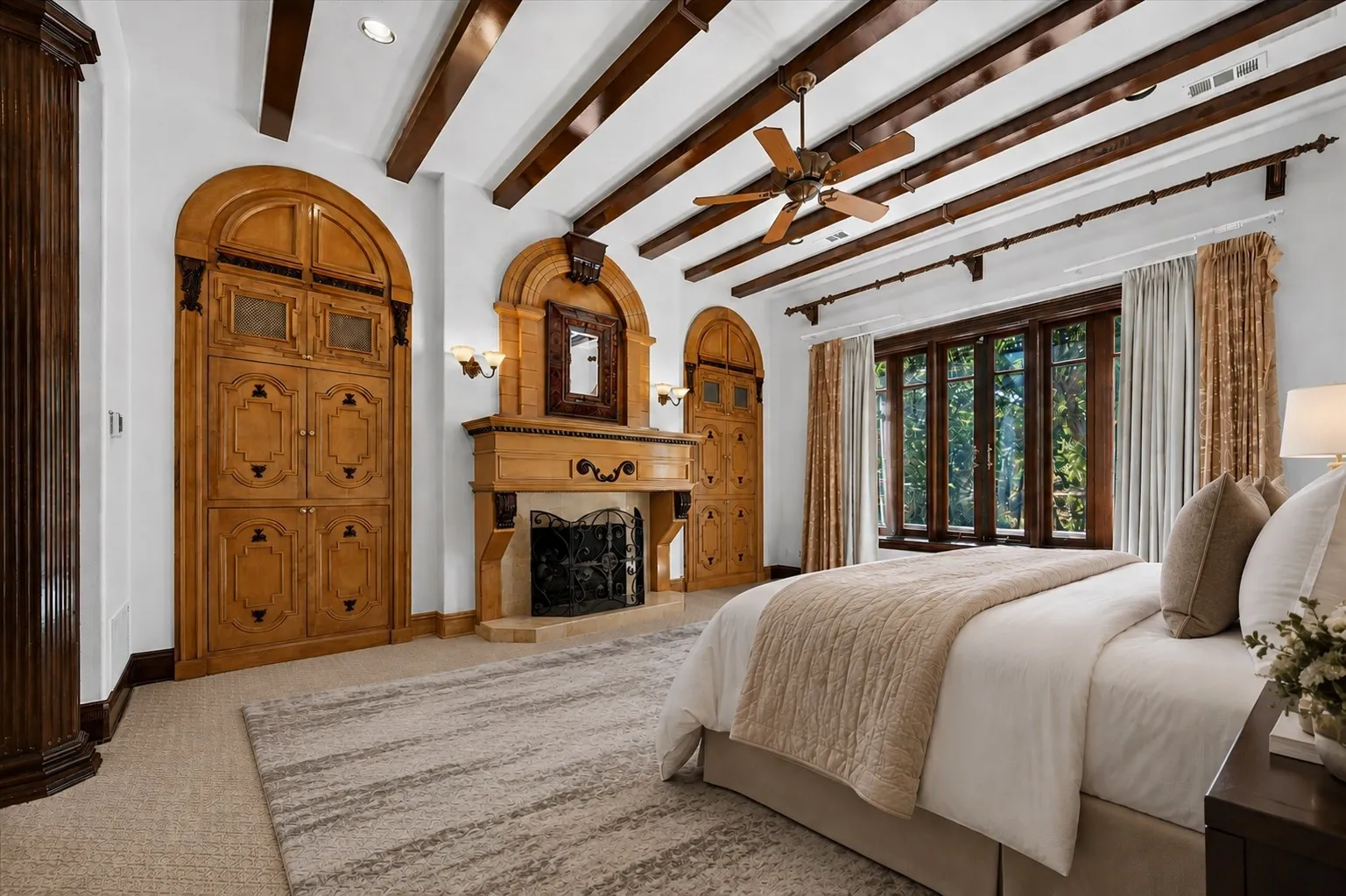 The lavish primary suite boasts a fireplace framed by built-ins, sitting area, soaking tub, oversized shower with dual heads, split vanities with a makeup area, dual toilets, two custom closets, and a huge exercise room. This photo has been virtually staged