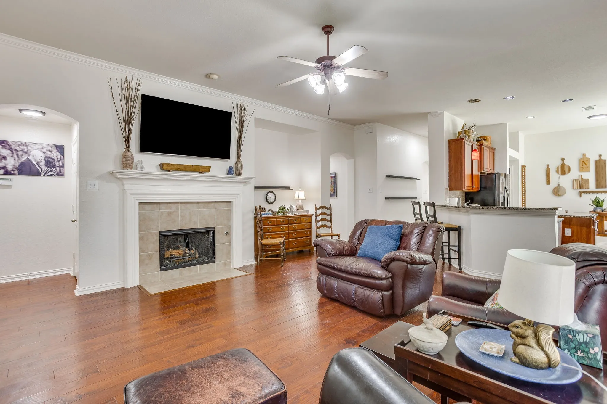 Spacious living area featuring wood-finish flooring, a fireplace with a tile surround and mantel, and a ceiling fan