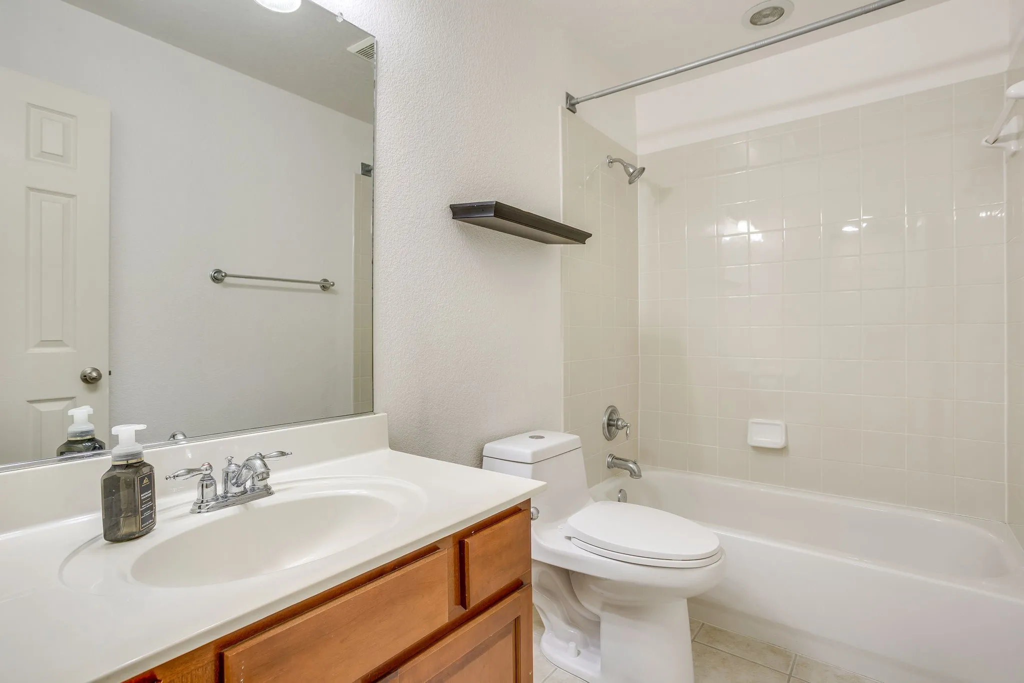 Bathroom featuring a vanity with an integrated sink, wood-finish cabinetry, a toilet, and a shower-over-tub combination with tiled walls