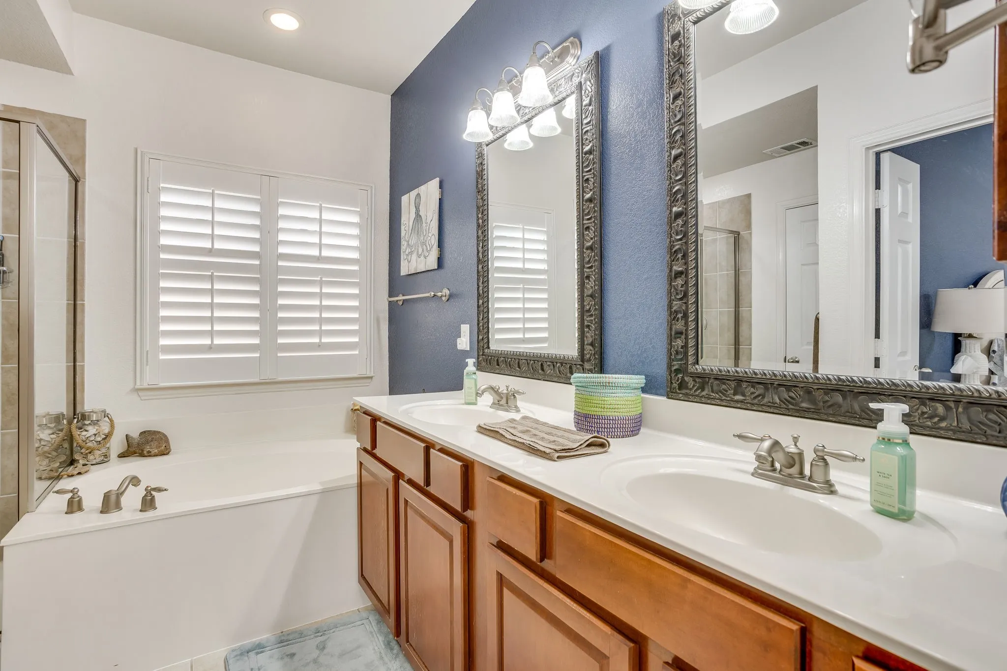Dual vanity with integrated sinks, framed mirrors, and a built-in tub with a window
