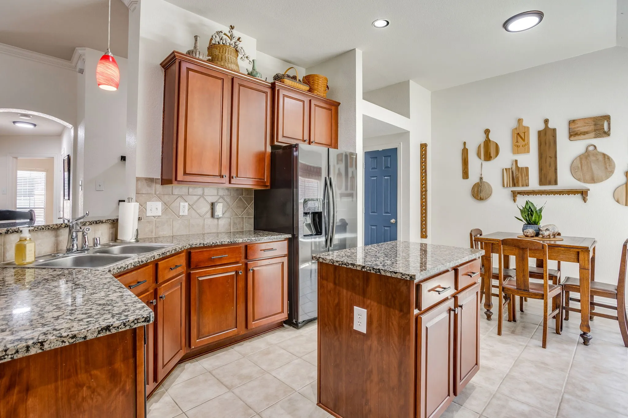 Kitchen featuring granite countertops, wood cabinetry, tile flooring, a stainless steel refrigerator, and a kitchen island
