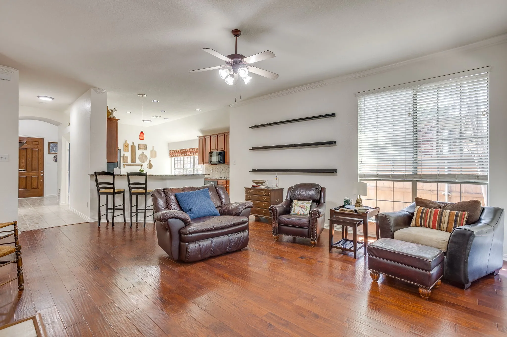 Wood-finish flooring throughout, ceiling fan with integrated lighting, built-in shelving, and a prominent window with blinds