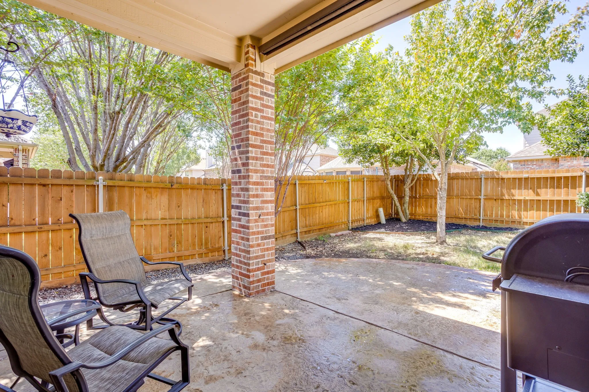 Covered patio with a concrete surface, brick column, and a wood privacy fence
