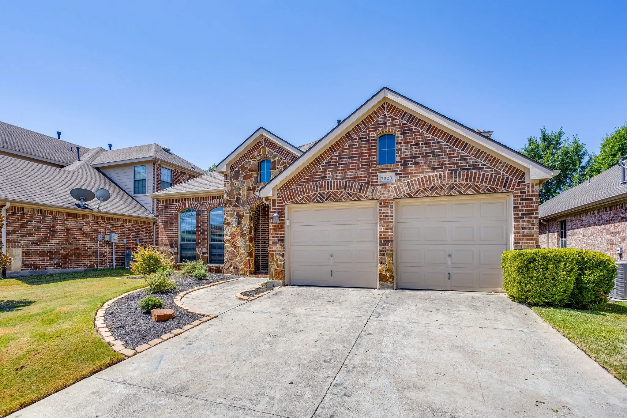 Brick and stone facade, two-car garage, concrete driveway, arched windows, landscaped entryway