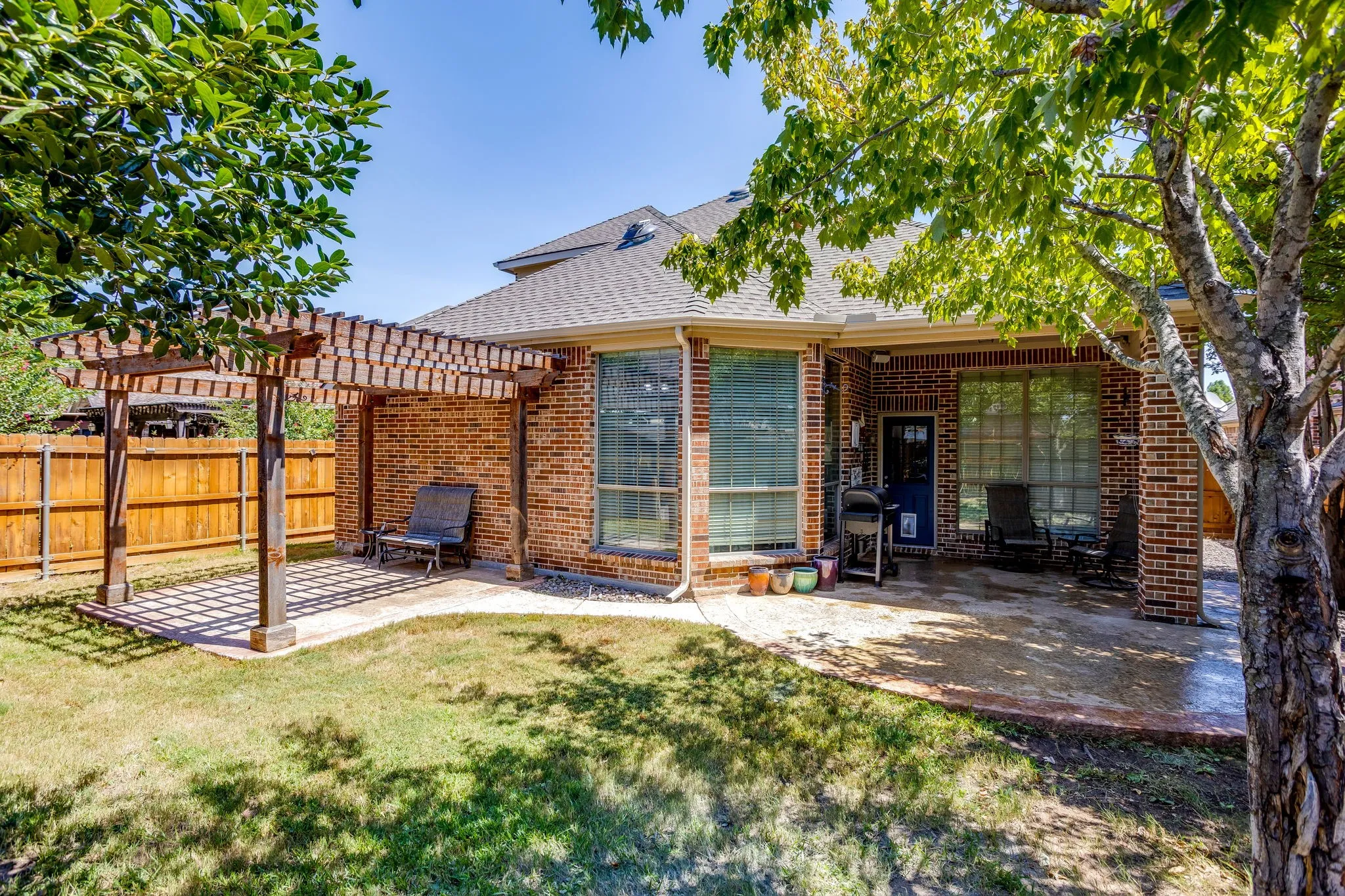 Brick exterior with a covered patio, a separate pergola, and a private wood fence