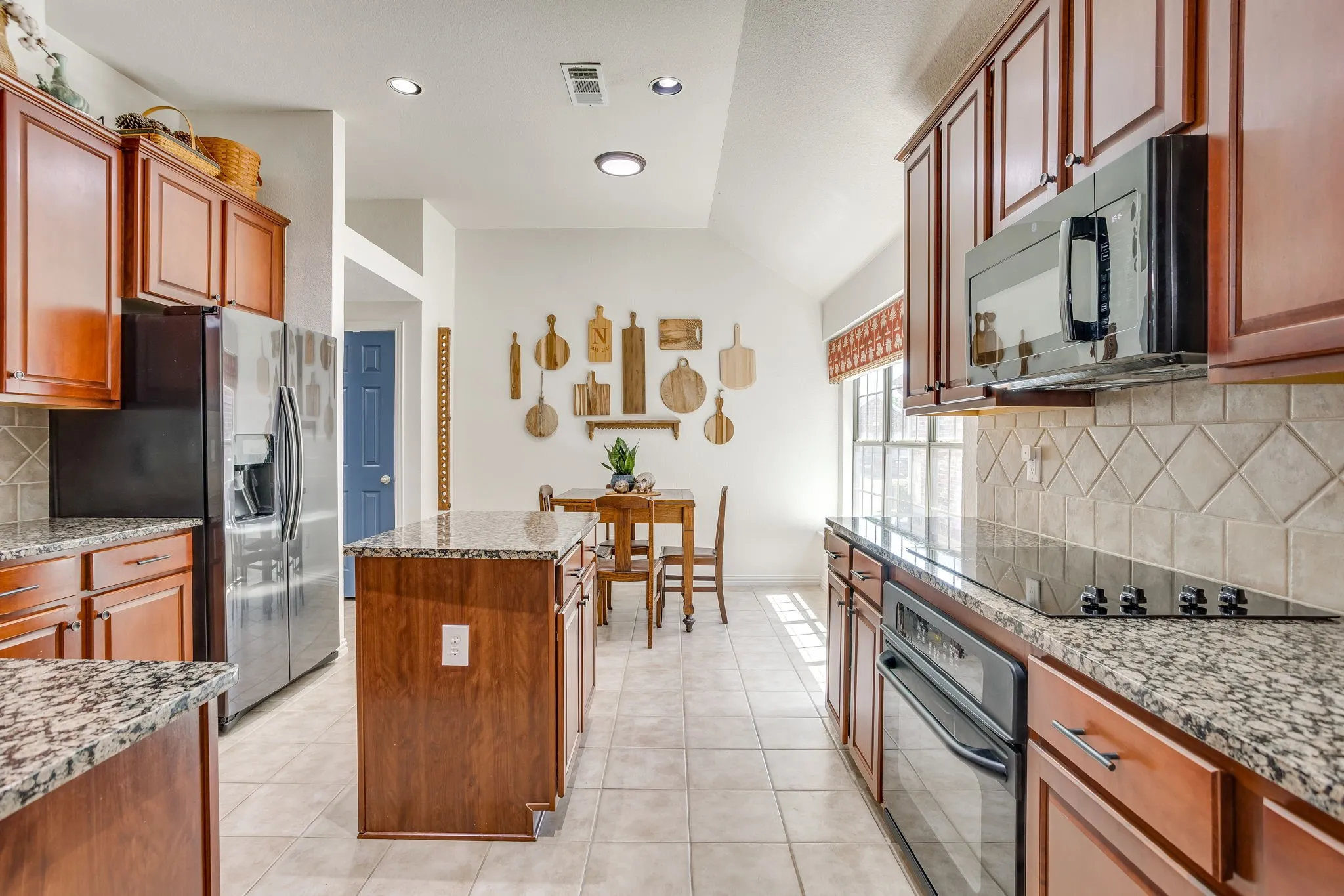 Kitchen featuring wood cabinetry, granite countertops, tile flooring, and stainless steel appliances including a refrigerator and built-in microwave